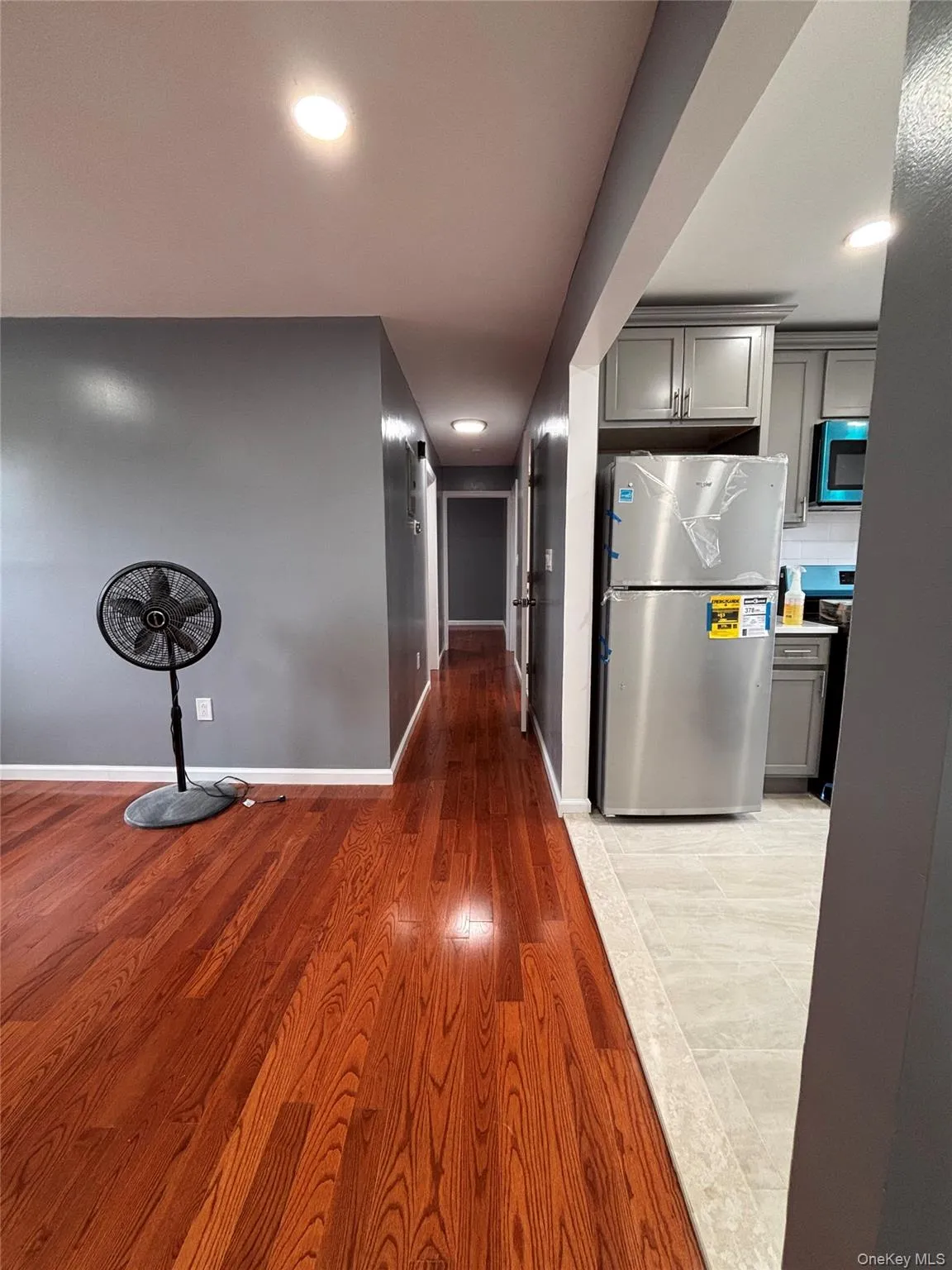 Hardwood flooring, recessed lighting, stainless steel refrigerator, and gray kitchen cabinetry Hardwood flooring, recessed lighting, stainless steel refrigerator, and gray kitchen cabinetry
