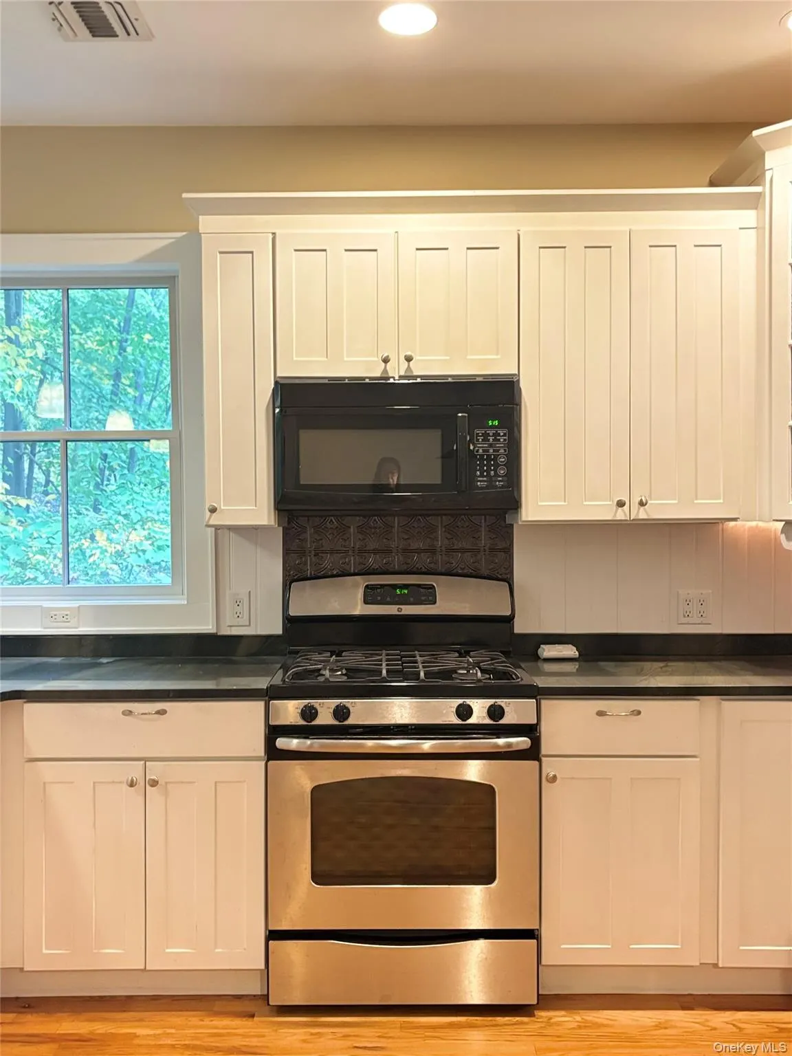 Stainless steel range with an overhead microwave, white shaker-style cabinetry, and stonecountertops Stainless steel range with an overhead microwave, white shaker-style cabinetry, and stonecountertops