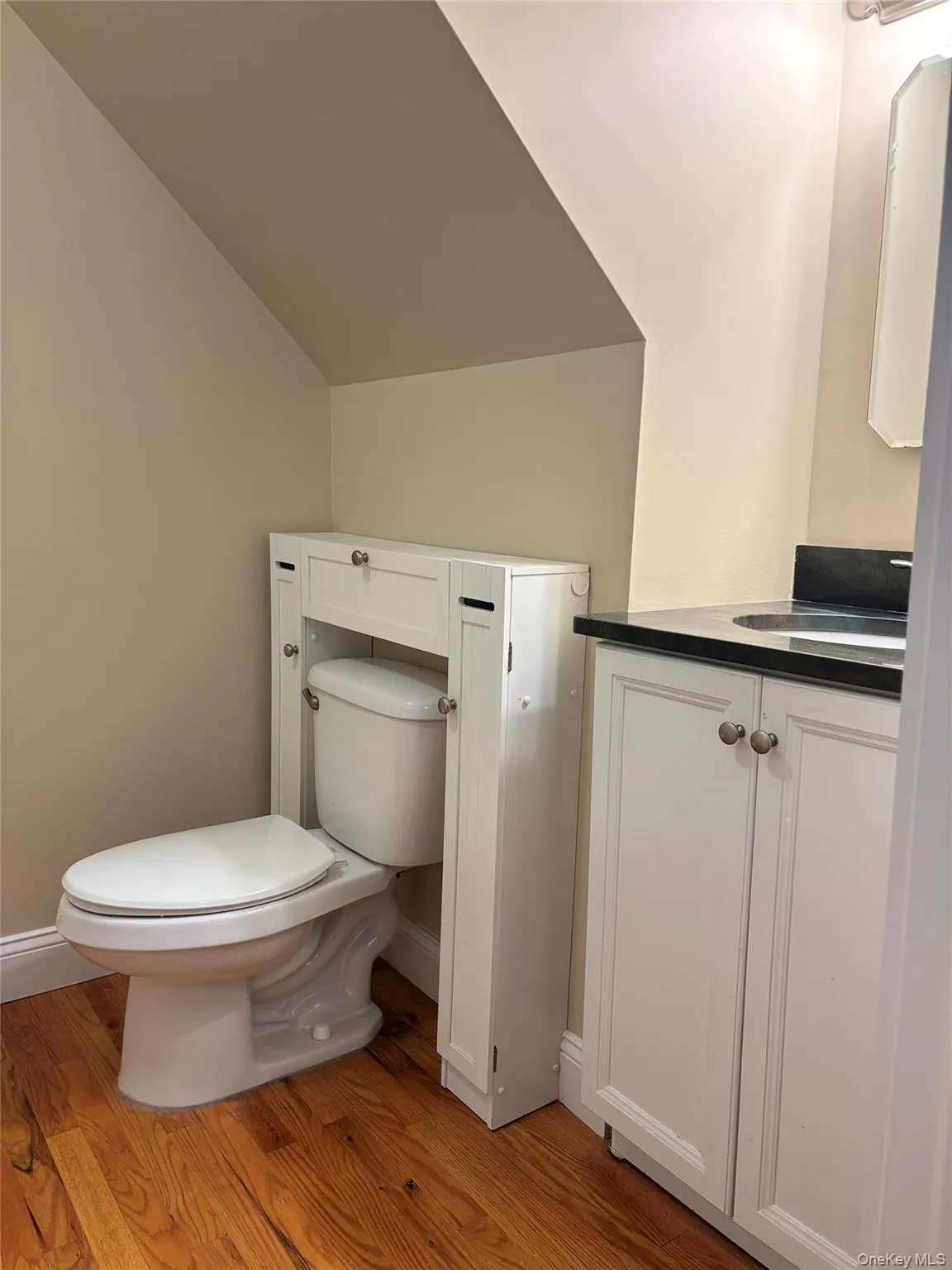Full bath on first floor has hardwood flooring which complements the white vanity with black stone countertop i with integrated sink Full bath on first floor has hardwood flooring which complements the white vanity with black stone countertop i with integrated sink
