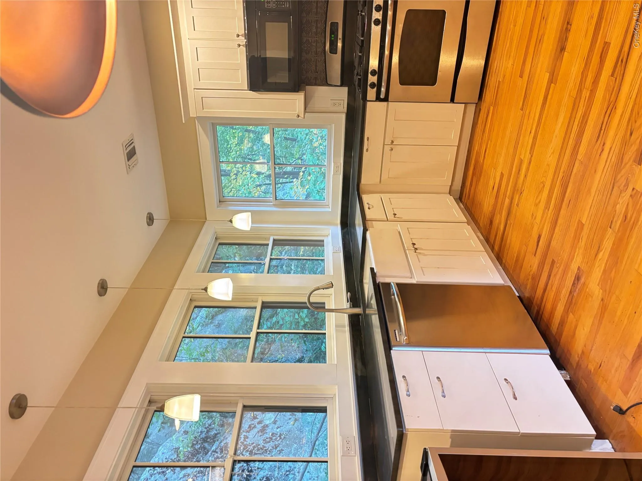 Kitchen featuring white cabinetry, dark countertops, wood-finish flooring, stainless steel appliances, and a farmhouse sink Kitchen featuring white cabinetry, dark countertops, wood-finish flooring, stainless steel appliances, and a farmhouse sink
