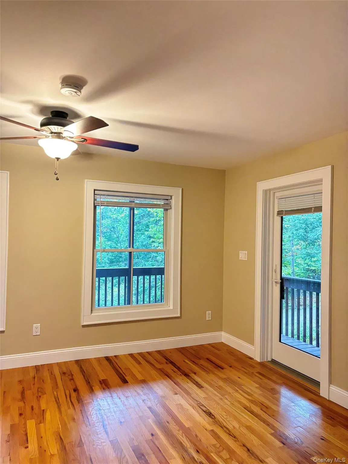1st floor bedroom has hardwood flooring throughout, a ceiling fan with integrated lighting, multiple windows, and a glass-paneled door opening to a private balcony 1st floor bedroom has hardwood flooring throughout, a ceiling fan with integrated lighting, multiple windows, and a glass-paneled door opening to a private balcony