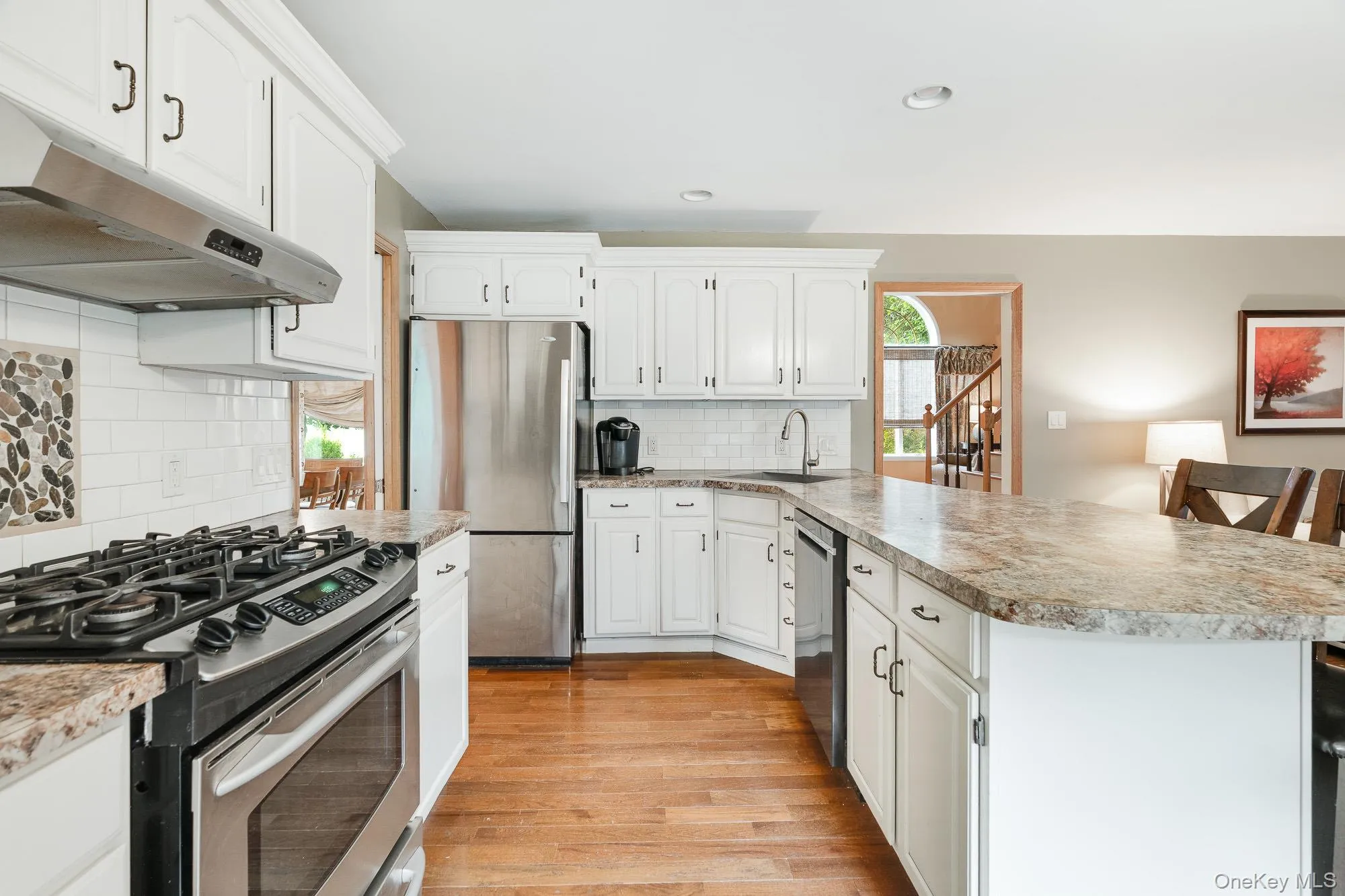 Kitchen featuring appliances with stainless steel finishes, white cabinets, light wood-type flooring, under cabinet range hood, and light countertops Kitchen featuring appliances with stainless steel finishes, white cabinets, light wood-type flooring, under cabinet range hood, and light countertops