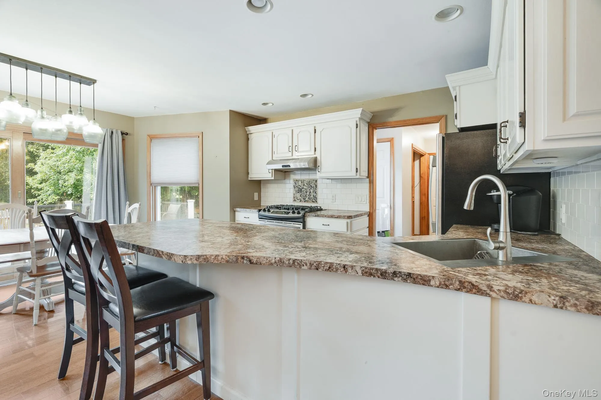 Kitchen featuring backsplash, white cabinets, stainless steel gas range, decorative light fixtures, and a breakfast bar Kitchen featuring backsplash, white cabinets, stainless steel gas range, decorative light fixtures, and a breakfast bar