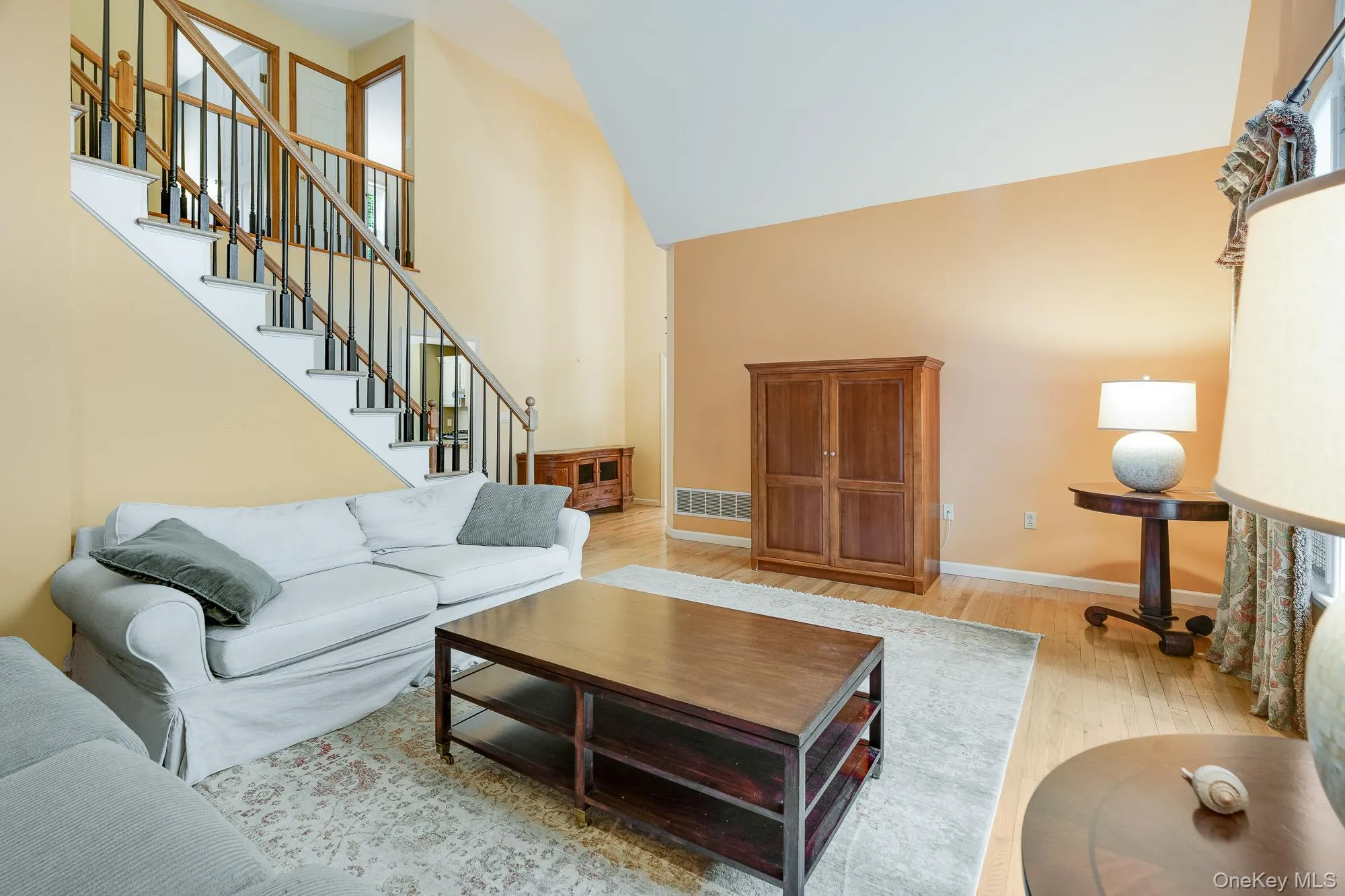 Living room featuring light wood-style flooring, high vaulted ceiling, and stairway Living room featuring light wood-style flooring, high vaulted ceiling, and stairway