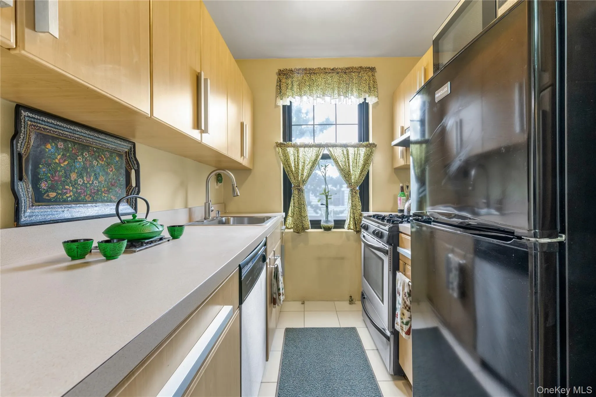 Kitchen featuring light wood-finish cabinetry, solid surface countertops, a stainless steel sink with a gooseneck faucet, a black refrigerator, and a stainless steel range Kitchen featuring light wood-finish cabinetry, solid surface countertops, a stainless steel sink with a gooseneck faucet, a black refrigerator, and a stainless steel range