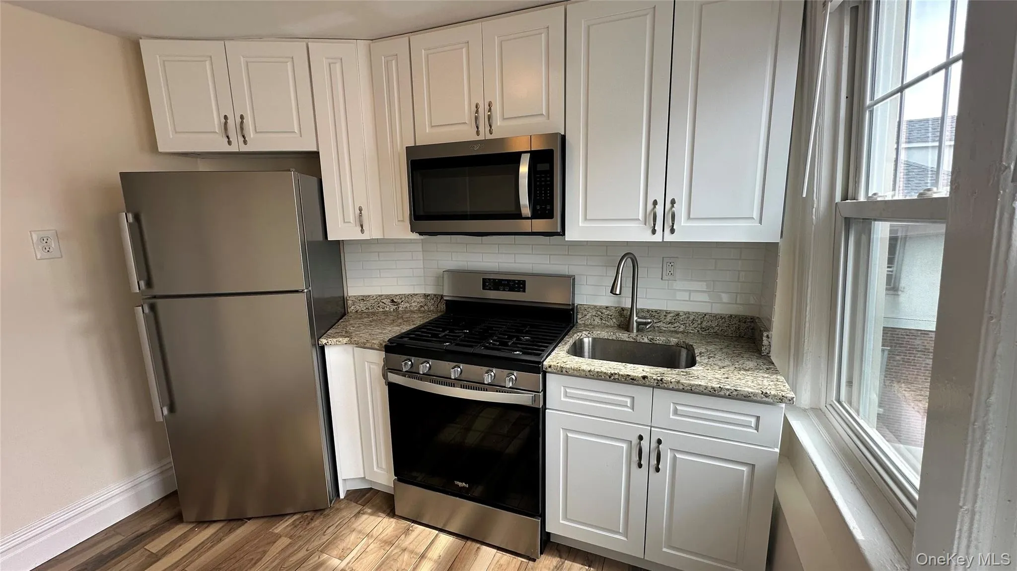 Kitchen featuring white cabinetry, stainless steel appliances, granite-style countertops, white subway tile backsplash, and wood-finish flooring Kitchen featuring white cabinetry, stainless steel appliances, granite-style countertops, white subway tile backsplash, and wood-finish flooring