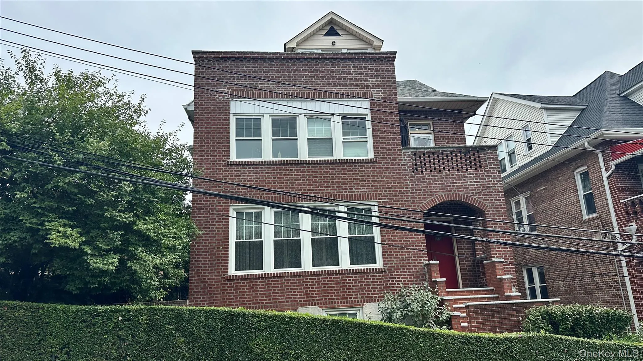 Brick exterior, arched entryway, upper balcony, multi-pane windows, and a mature hedge Brick exterior, arched entryway, upper balcony, multi-pane windows, and a mature hedge