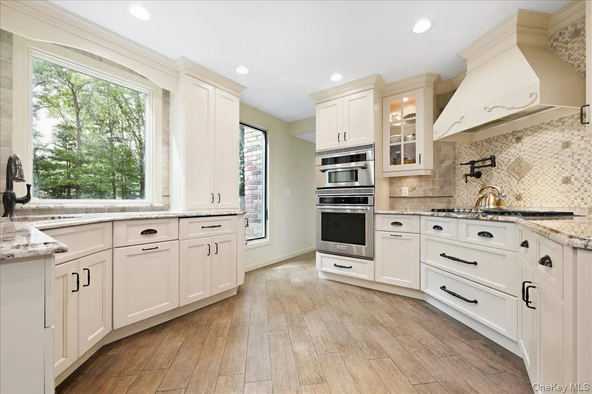 White cabinetry with dark hardware, granite countertops, tile backsplash, built-in stainless steel appliances White cabinetry with dark hardware, granite countertops, tile backsplash, built-in stainless steel appliances