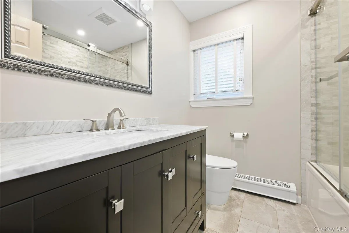 Bathroom featuring a dark wood vanity with a white countertop, brushed nickel faucet, large decorative mirror, and tiled flooring Bathroom featuring a dark wood vanity with a white countertop, brushed nickel faucet, large decorative mirror, and tiled flooring
