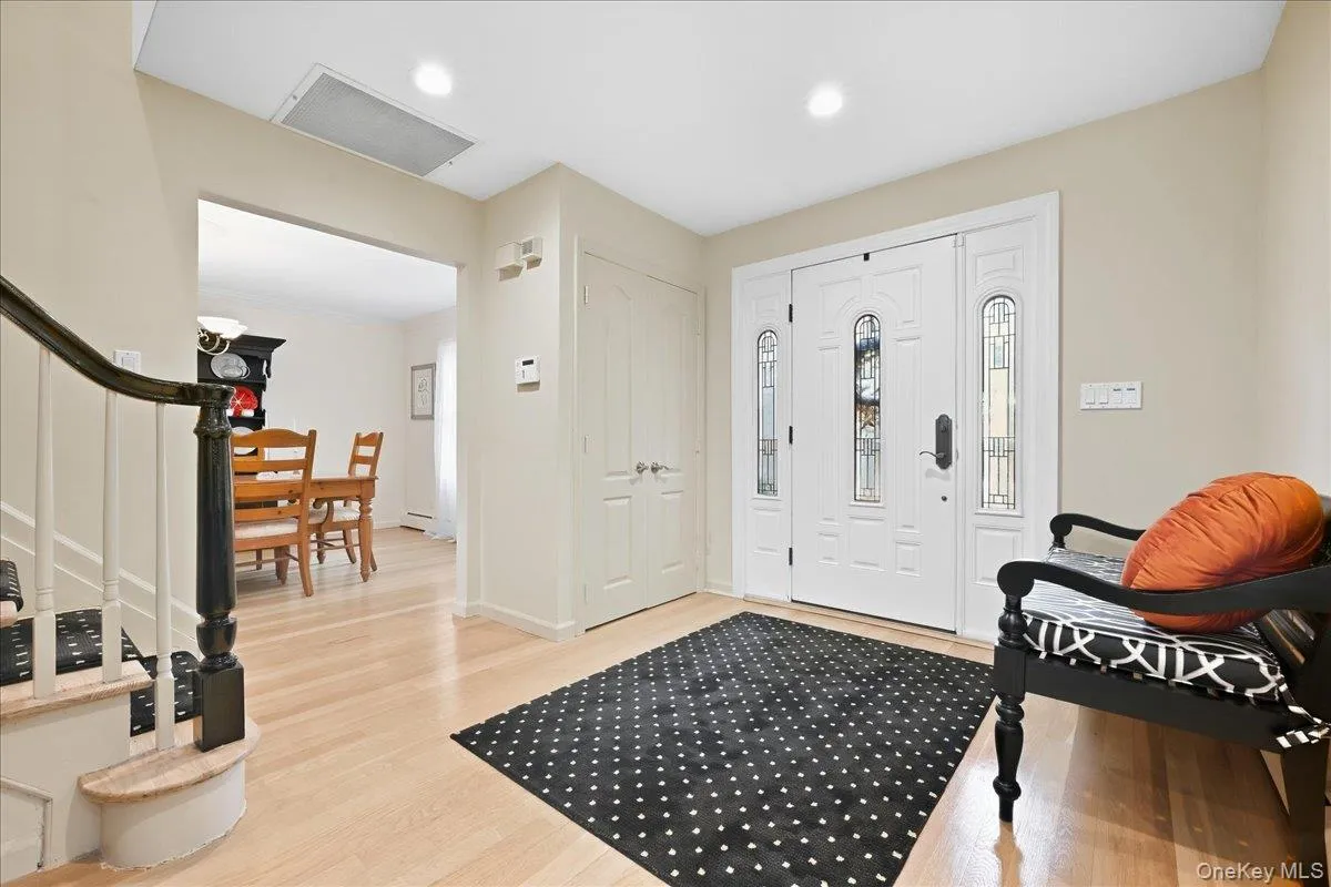 Entryway featuring wood-finish flooring, white paneled doors, and a staircase with a dark wood handrail Entryway featuring wood-finish flooring, white paneled doors, and a staircase with a dark wood handrail