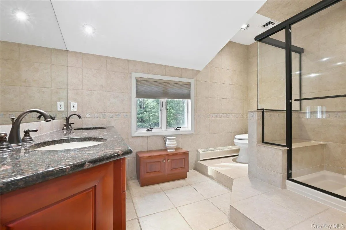 Dual vanity with dark stone countertop, glass-enclosed shower, built-in shower bench, and recessed lighting Dual vanity with dark stone countertop, glass-enclosed shower, built-in shower bench, and recessed lighting