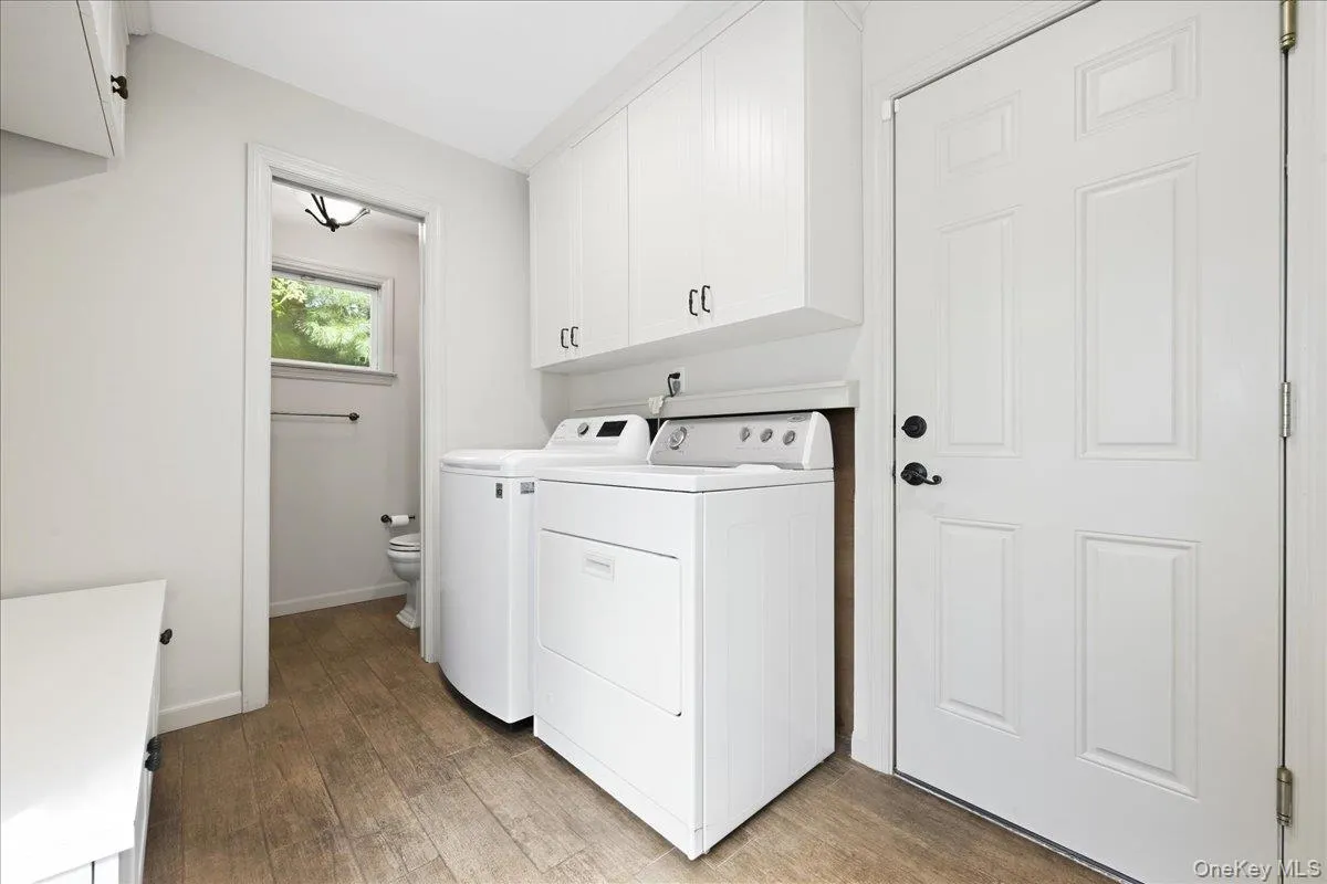 Laundry area featuring wood-finish flooring, white cabinetry, and a white paneled door. Laundry area featuring wood-finish flooring, white cabinetry, and a white paneled door.