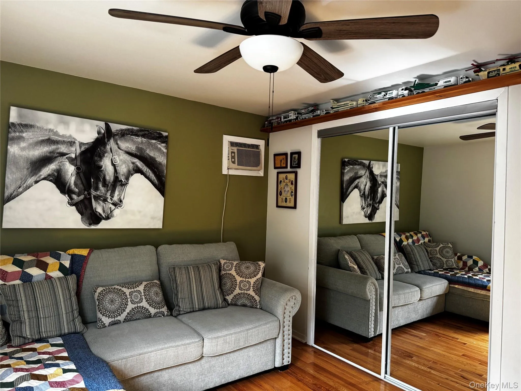 Wood-finish flooring, ceiling fan with light fixture, mirrored closet doors, and a built-in air conditioning unit Wood-finish flooring, ceiling fan with light fixture, mirrored closet doors, and a built-in air conditioning unit