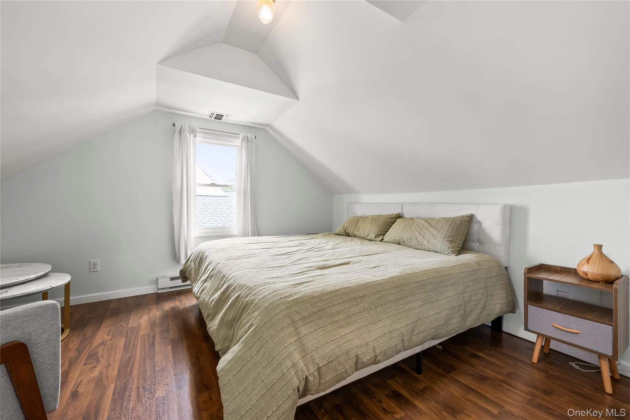 Sloped ceilings with a dormer, wood-finish flooring, and natural light from a single window Sloped ceilings with a dormer, wood-finish flooring, and natural light from a single window