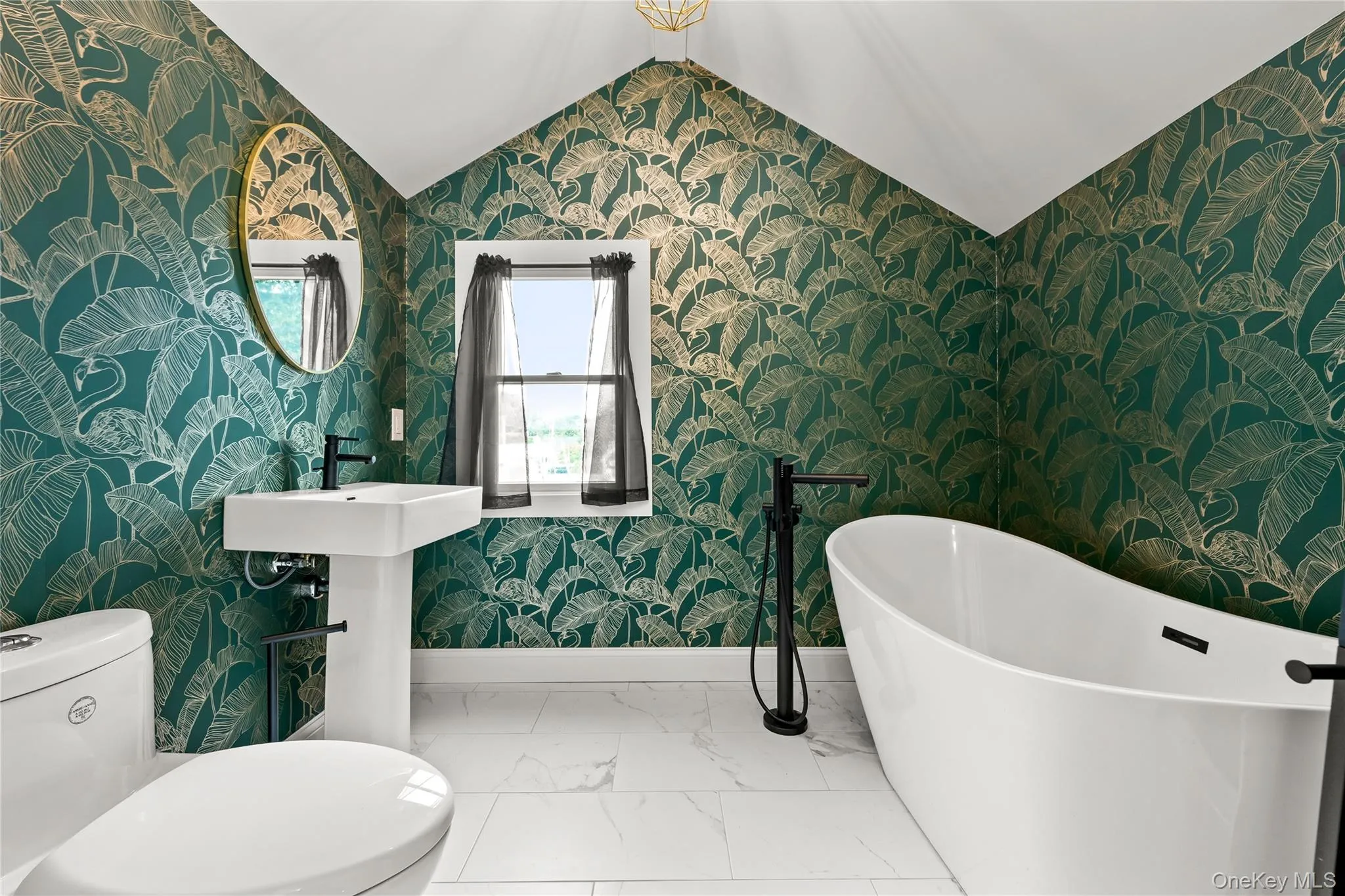 Pedestal sink with a matte black faucet, a freestanding bathtub with a floor-mounted fixture, and white tile flooring Pedestal sink with a matte black faucet, a freestanding bathtub with a floor-mounted fixture, and white tile flooring