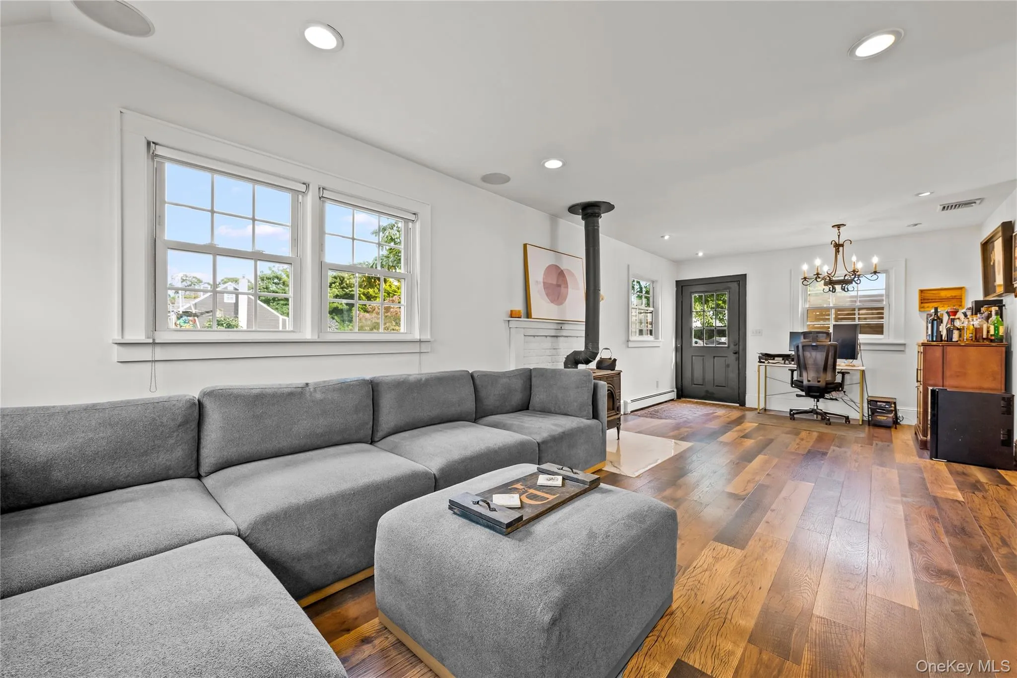 Wood-finish flooring, recessed ceiling lighting, a wood-burning stove with a decorative mantle, and white trim windows Wood-finish flooring, recessed ceiling lighting, a wood-burning stove with a decorative mantle, and white trim windows