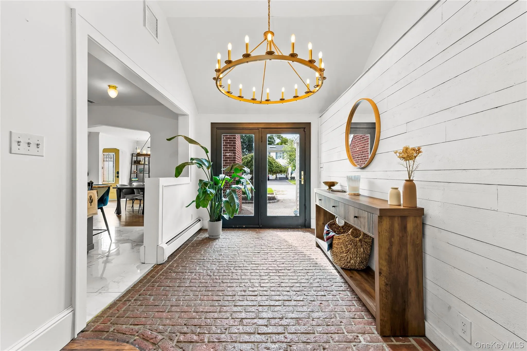 Brick flooring, vaulted white ceiling, shiplap wall, brass chandelier, and double entry doors Brick flooring, vaulted white ceiling, shiplap wall, brass chandelier, and double entry doors
