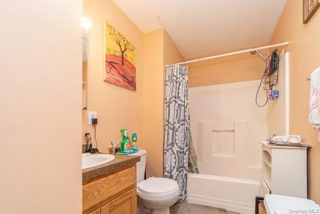 Bathroom featuring a wood-finish vanity with an integrated sink, a commode, and a shower-tub combination Bathroom featuring a wood-finish vanity with an integrated sink, a commode, and a shower-tub combination