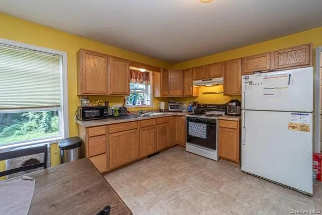Kitchen featuring wood-finish cabinetry, laminate countertops, a built-in range with an overhead microwave, and resilient flooring Kitchen featuring wood-finish cabinetry, laminate countertops, a built-in range with an overhead microwave, and resilient flooring