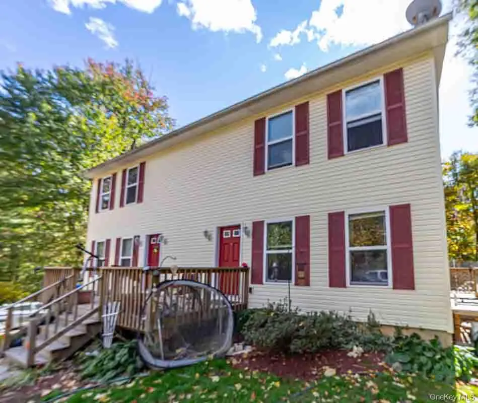 Two-story exterior with light-colored siding, multiple windows with red shutters, and a front deck with stairs Two-story exterior with light-colored siding, multiple windows with red shutters, and a front deck with stairs