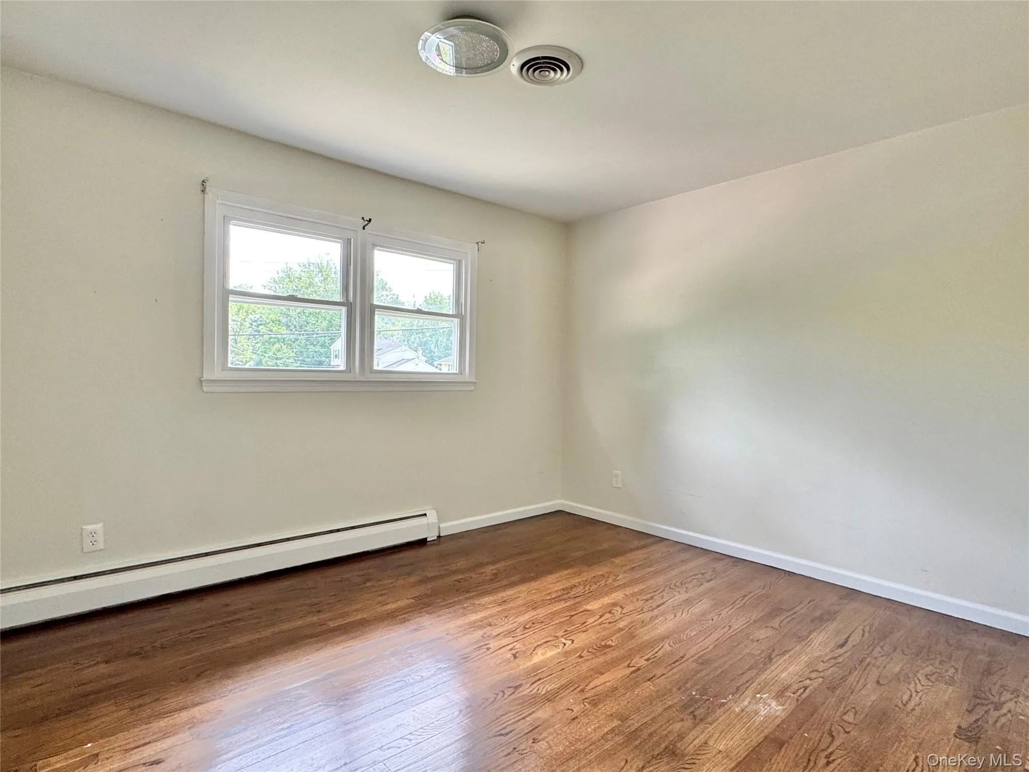 Spare room featuring wood finished floors and a baseboard radiator Spare room featuring wood finished floors and a baseboard radiator