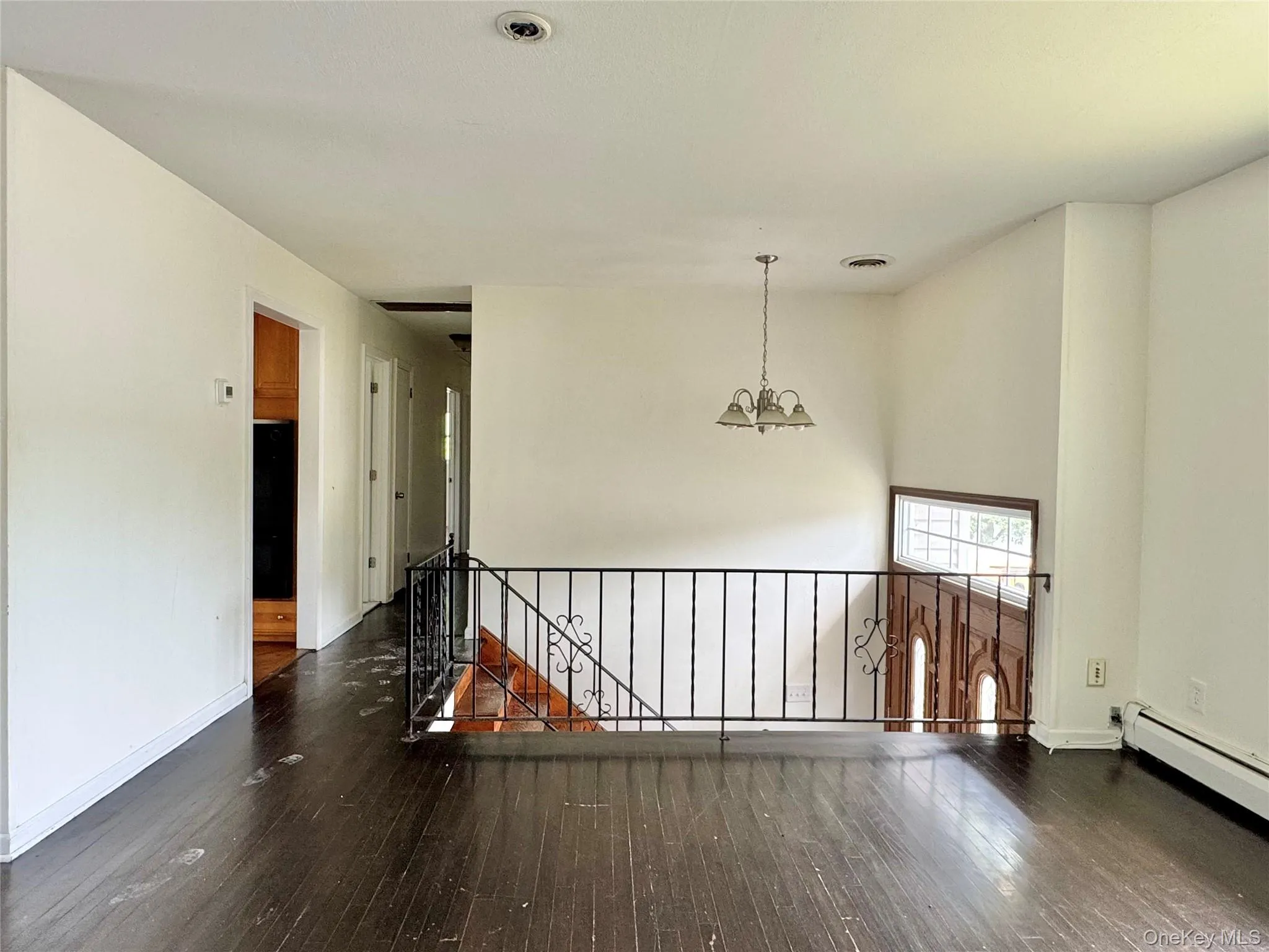 Empty room with a chandelier, hardwood / wood-style floors, and baseboard heating Empty room with a chandelier, hardwood / wood-style floors, and baseboard heating