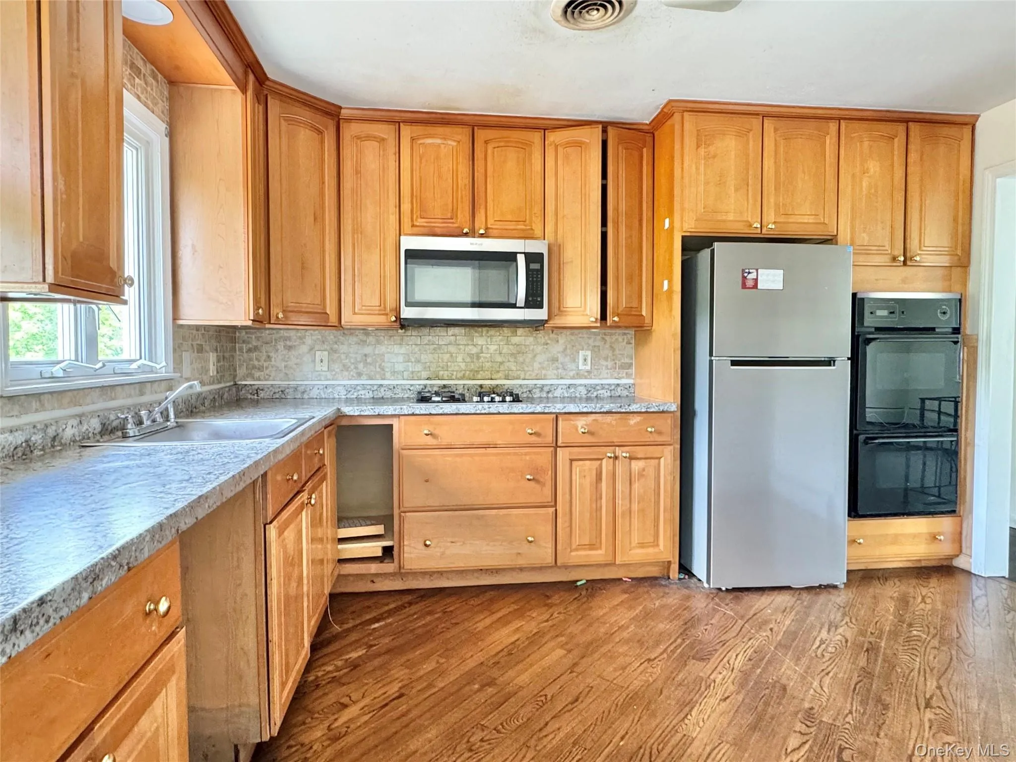 Kitchen with wood finished floors, stainless steel appliances, decorative backsplash, and light countertops Kitchen with wood finished floors, stainless steel appliances, decorative backsplash, and light countertops
