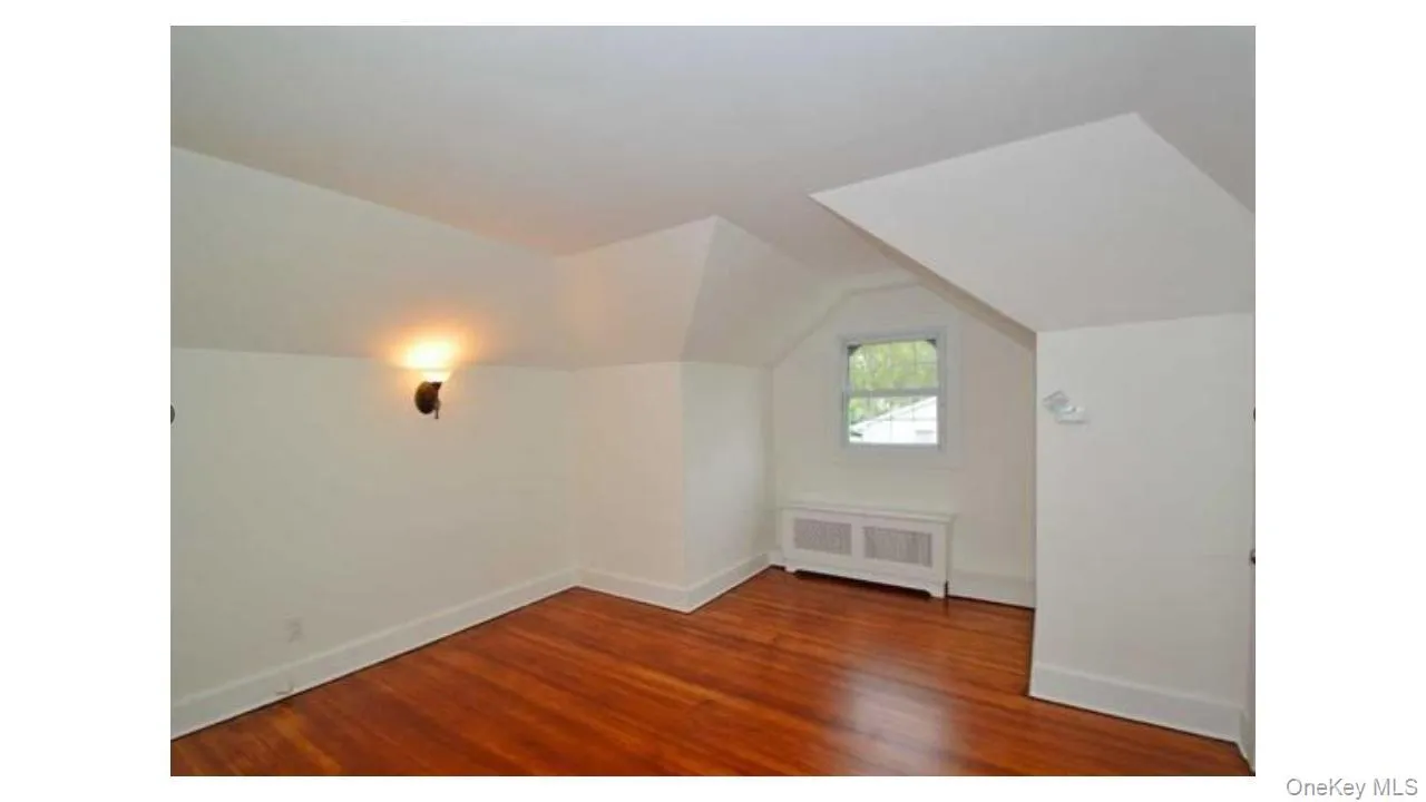 Hardwood flooring, painted white trim, window, wall-mounted sconce, and radiator cover Hardwood flooring, painted white trim, window, wall-mounted sconce, and radiator cover