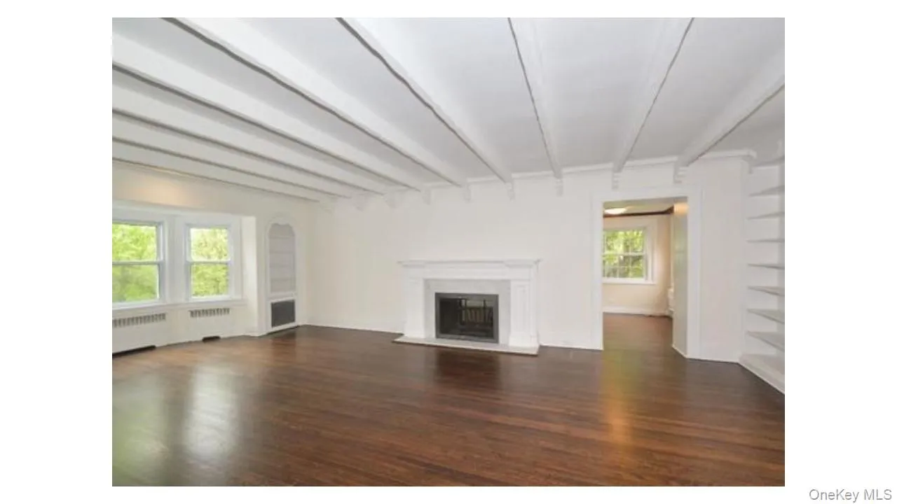 Exposed ceiling beams, rich wood-finish flooring, a classic fireplace with a stone surround, built-in shelving, and a bay window Exposed ceiling beams, rich wood-finish flooring, a classic fireplace with a stone surround, built-in shelving, and a bay window