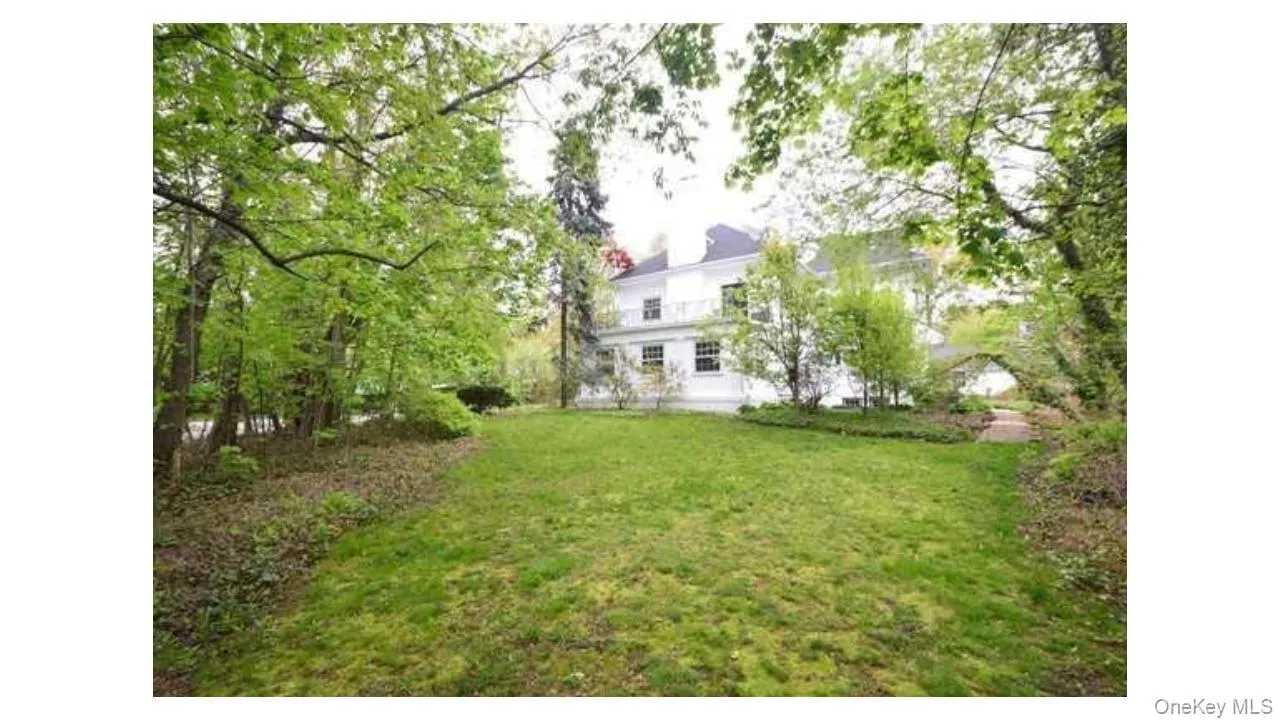 Expansive lawn surrounded by mature trees, featuring a white multi-story residence with multiple windows and a balcony Expansive lawn surrounded by mature trees, featuring a white multi-story residence with multiple windows and a balcony