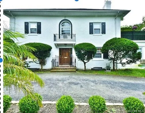 White stucco exterior with black functional shutters, front entry with transom window, second-story Juliet balcony, and paved driveway White stucco exterior with black functional shutters, front entry with transom window, second-story Juliet balcony, and paved driveway