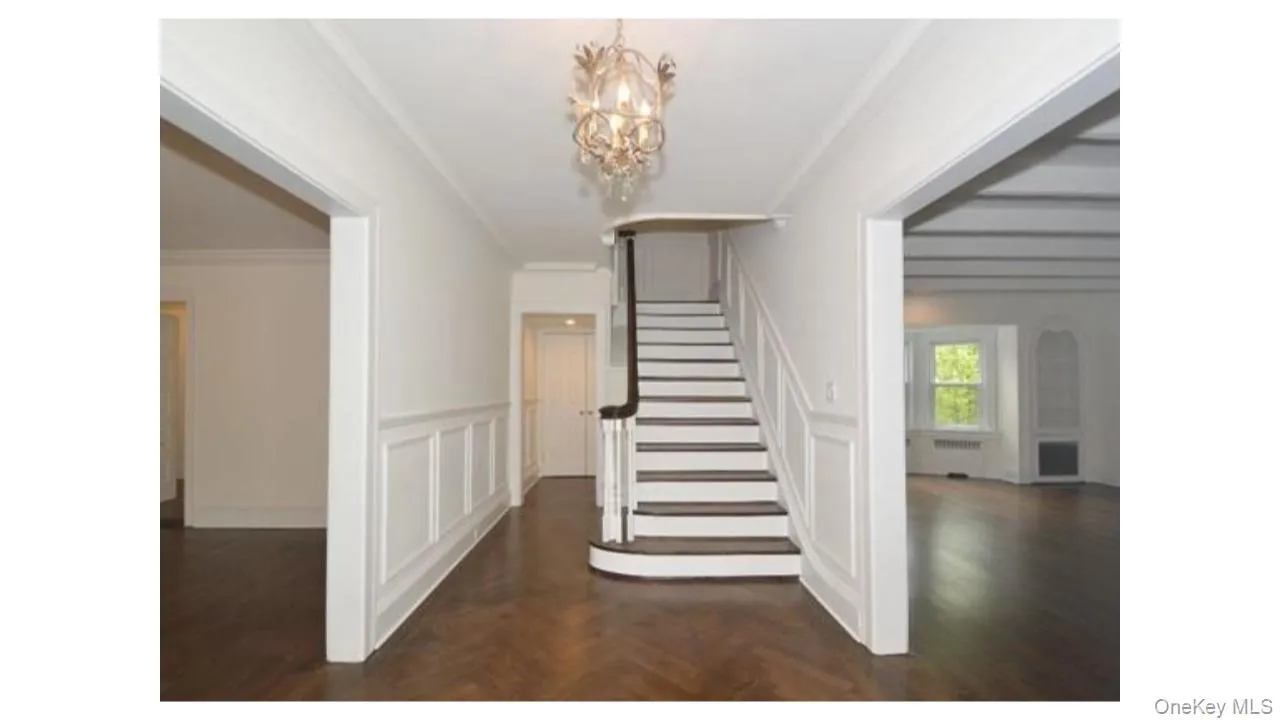Wood-finish flooring, staircase with dark wood handrail, decorative chandelier, wainscoting paneling, and coffered ceilings Wood-finish flooring, staircase with dark wood handrail, decorative chandelier, wainscoting paneling, and coffered ceilings