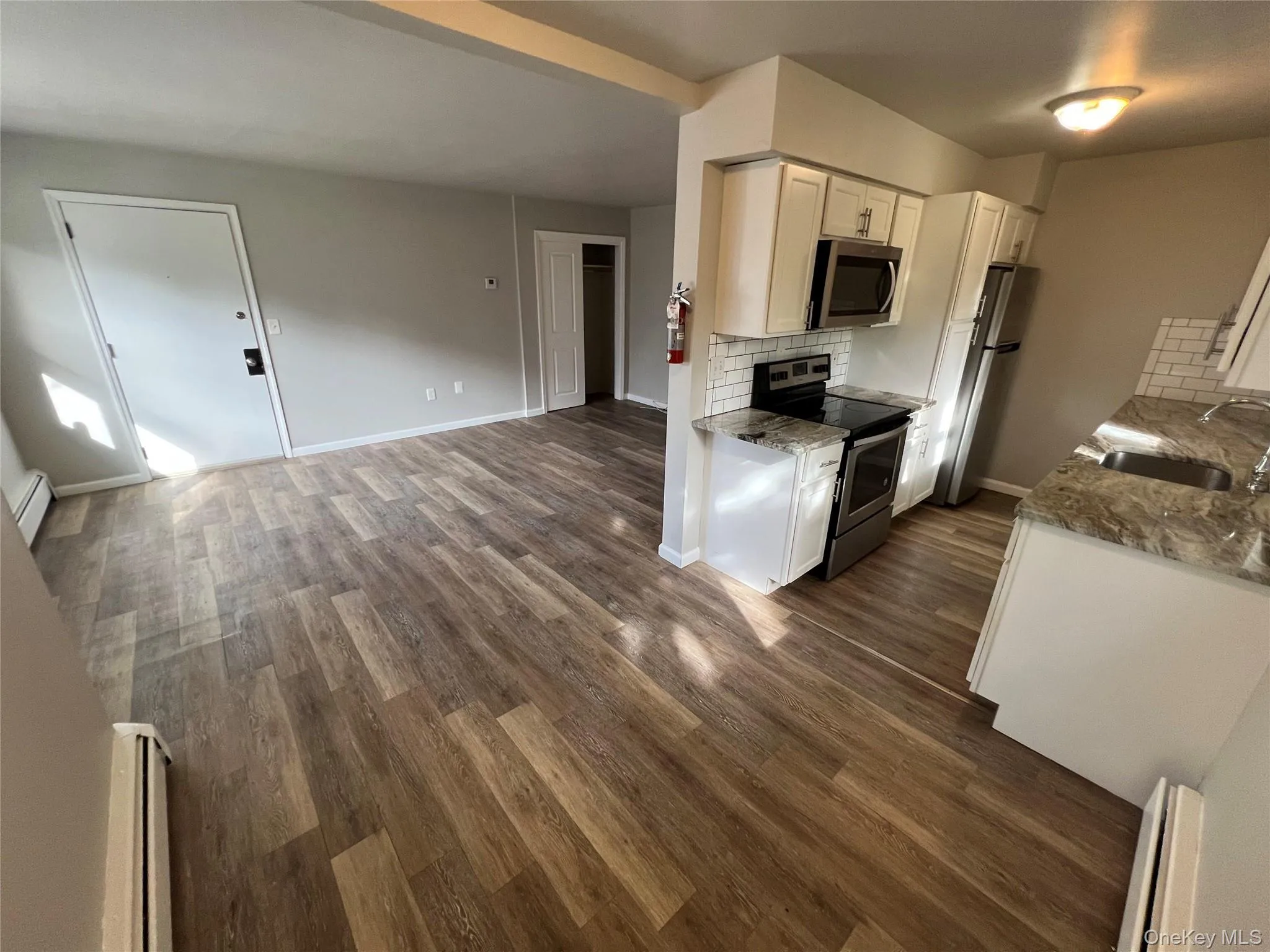 Wood-finish flooring, white cabinetry, stainless steel appliances, subway tile backsplash, and light-toned walls Wood-finish flooring, white cabinetry, stainless steel appliances, subway tile backsplash, and light-toned walls
