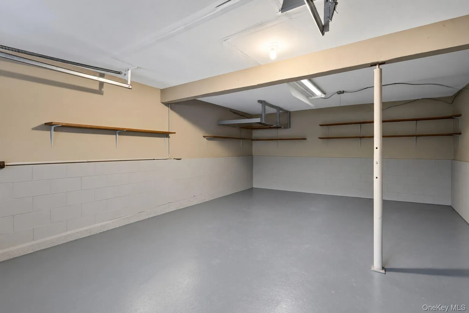 Concrete block walls with painted finish, gray painted concrete flooring, and multiple wood-finish shelving units Concrete block walls with painted finish, gray painted concrete flooring, and multiple wood-finish shelving units