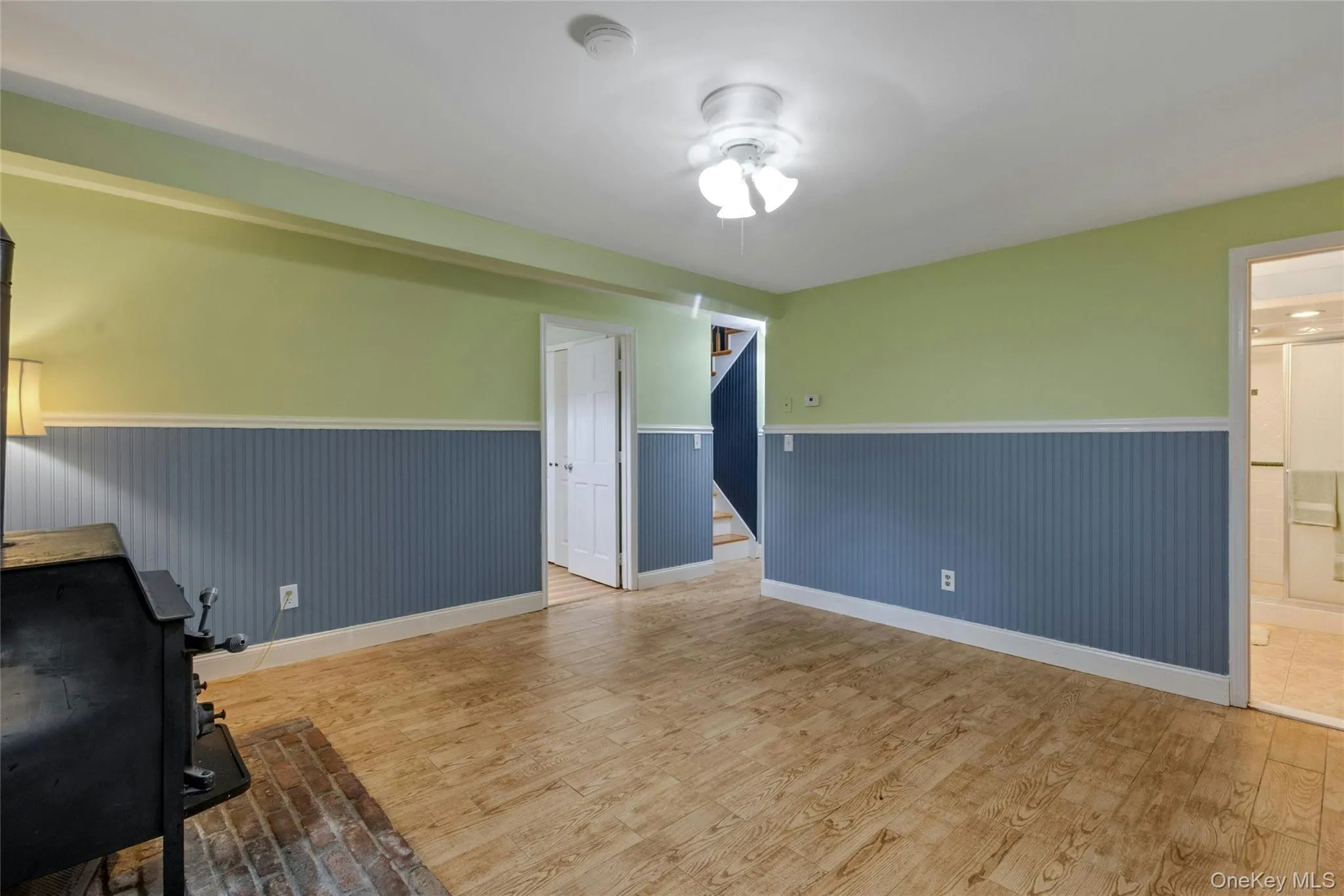 Wood-finish flooring with a ceiling fan, built-in shelving, windows, and a wood-burning stove with a brick hearth Wood-finish flooring with a ceiling fan, built-in shelving, windows, and a wood-burning stove with a brick hearth