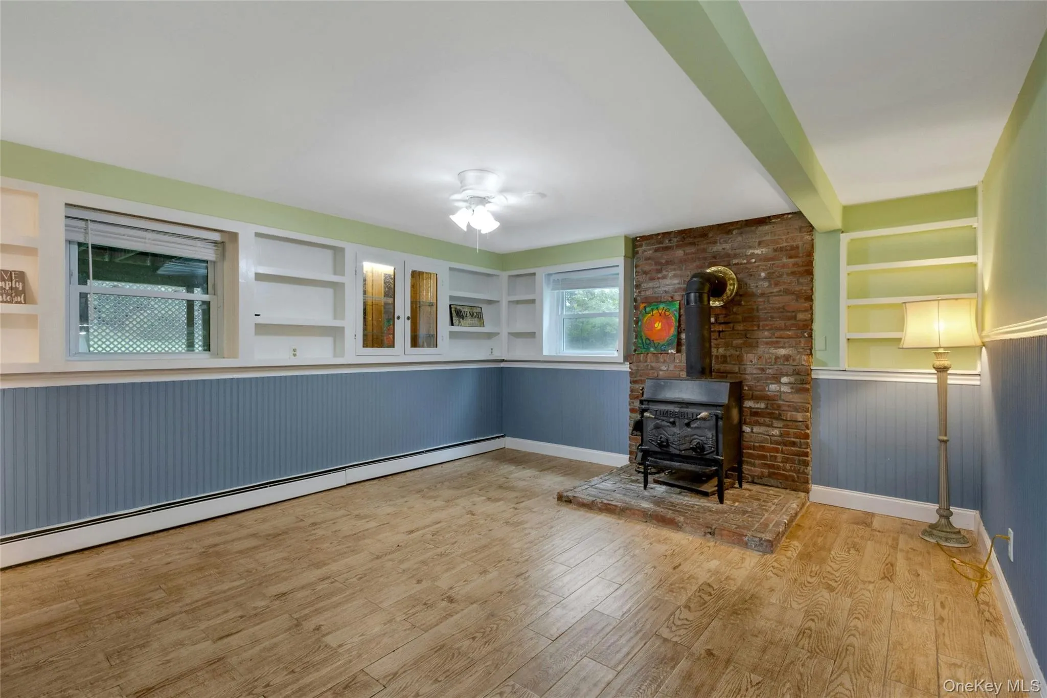 Wood-finish flooring, built-in shelving, a brick-surround wood stove, and paneled wall accents Wood-finish flooring, built-in shelving, a brick-surround wood stove, and paneled wall accents