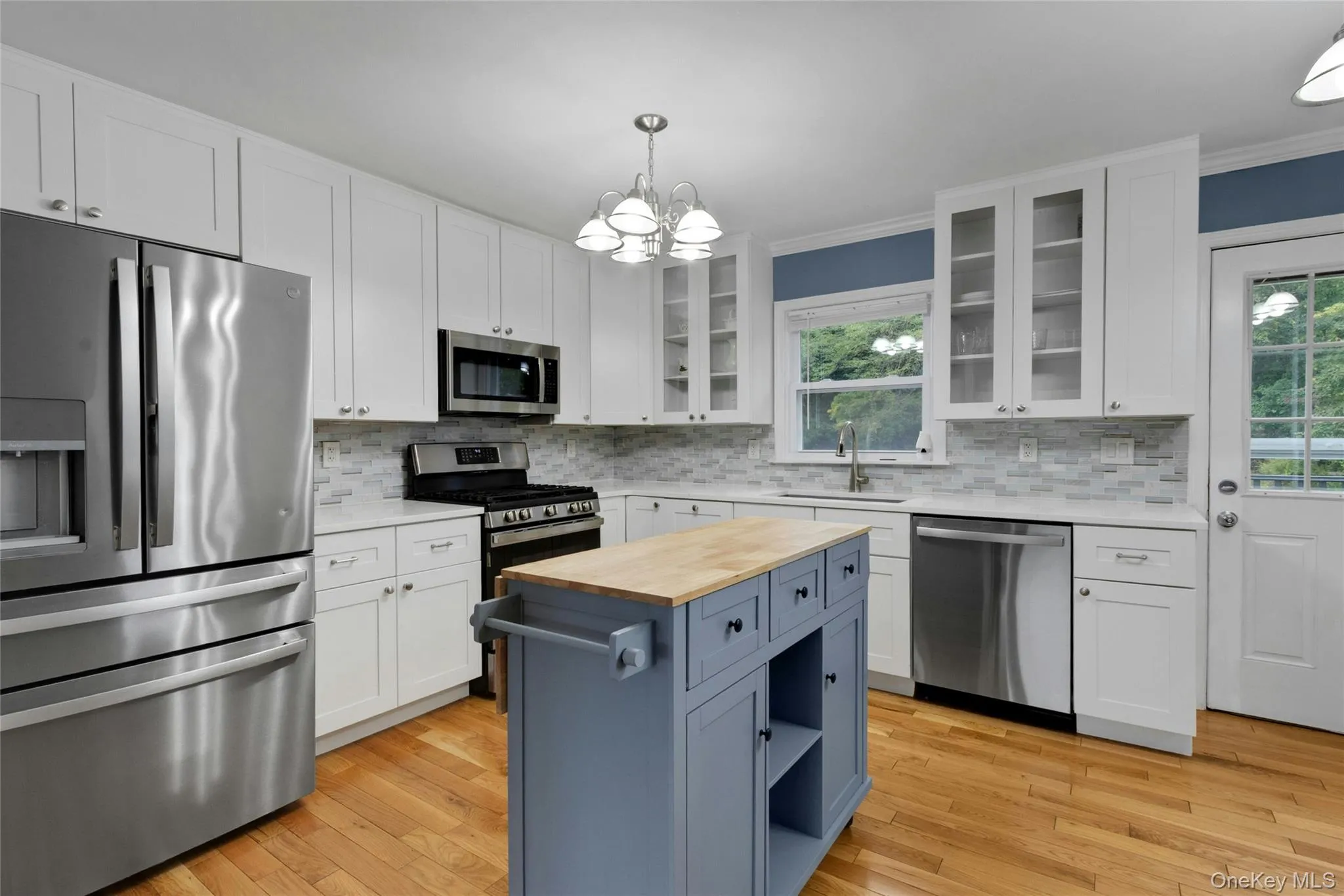 Kitchen featuring light wood-finish flooring, white cabinetry, stainless steel appliances, a tile backsplash, and a central island with a wood countertop Kitchen featuring light wood-finish flooring, white cabinetry, stainless steel appliances, a tile backsplash, and a central island with a wood countertop