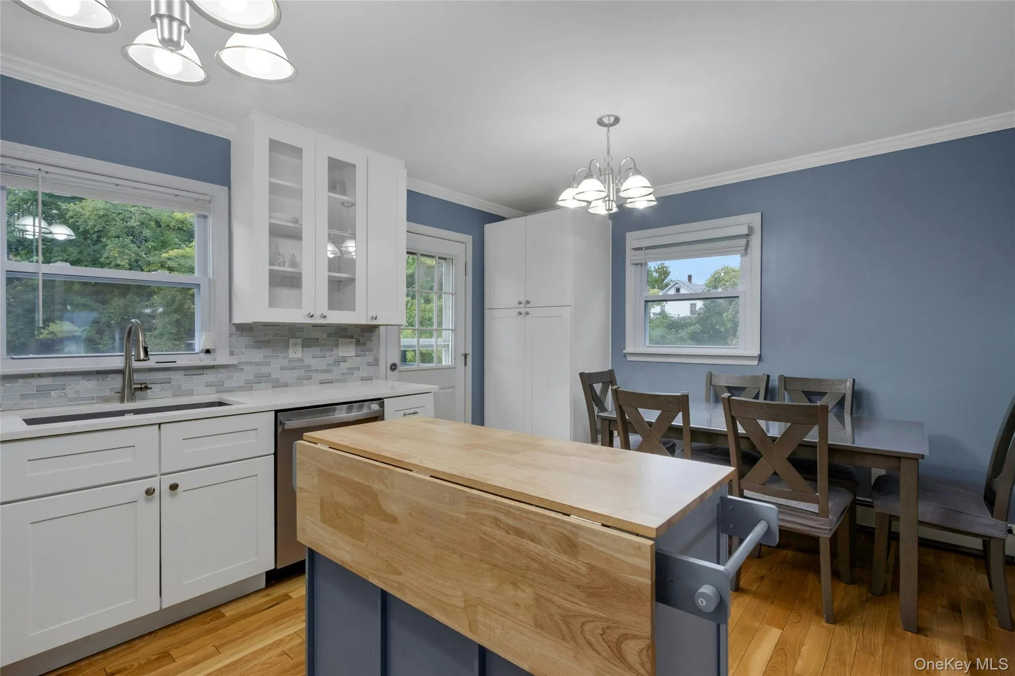 White cabinetry with glass-front uppers, stainless steel sink, and mosaic tile backsplash White cabinetry with glass-front uppers, stainless steel sink, and mosaic tile backsplash