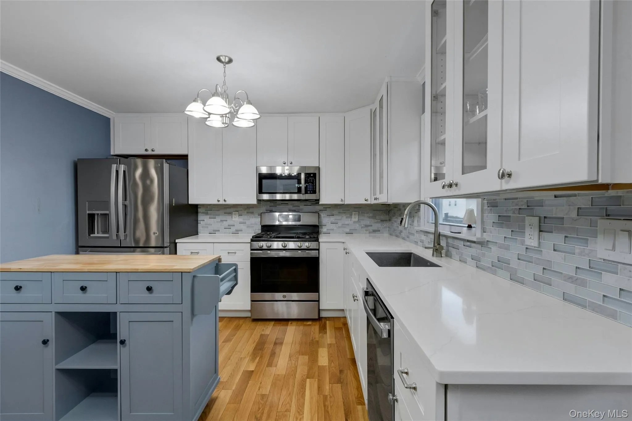 Kitchen featuring stainless steel appliances, white cabinetry, wood-finish flooring, a mosaic tile backsplash, and light-toned countertops Kitchen featuring stainless steel appliances, white cabinetry, wood-finish flooring, a mosaic tile backsplash, and light-toned countertops