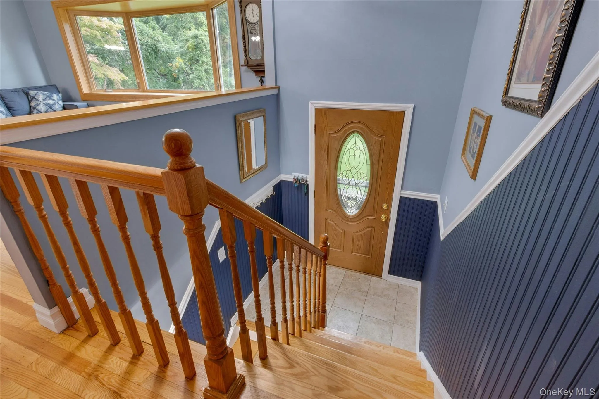 Hardwood staircase with natural wood railing, bay window, wood-finish flooring, and a decorative front door with an oval leaded glass insert Hardwood staircase with natural wood railing, bay window, wood-finish flooring, and a decorative front door with an oval leaded glass insert