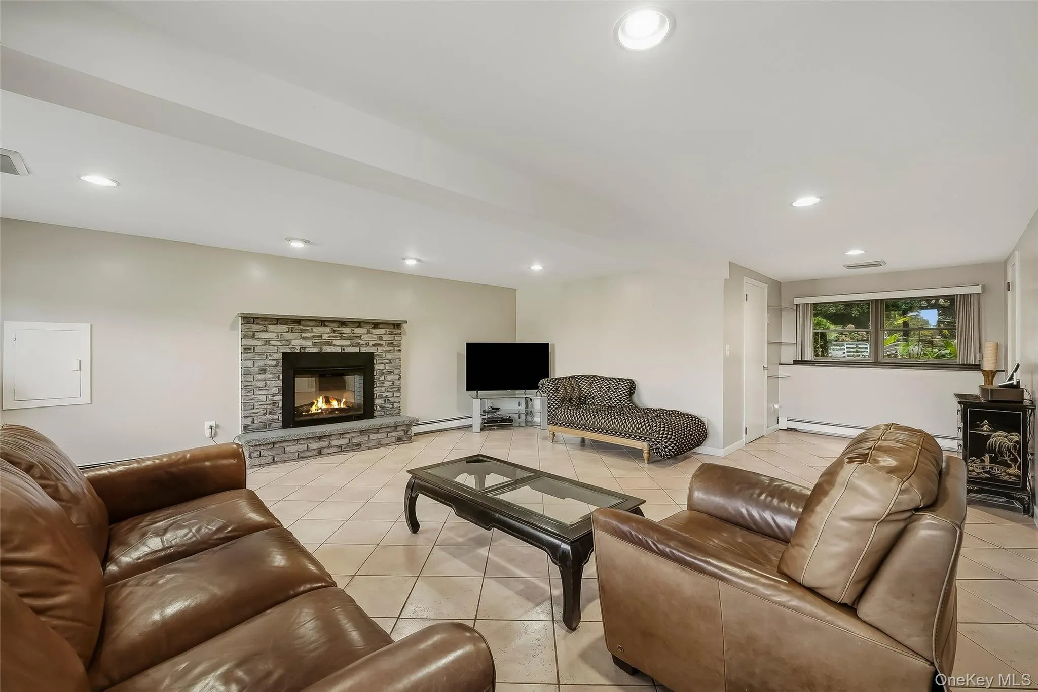 Tile flooring, stone-faced fireplace with hearth, recessed lighting, and window overlooking the backyard. Tile flooring, stone-faced fireplace with hearth, recessed lighting, and window overlooking the backyard.