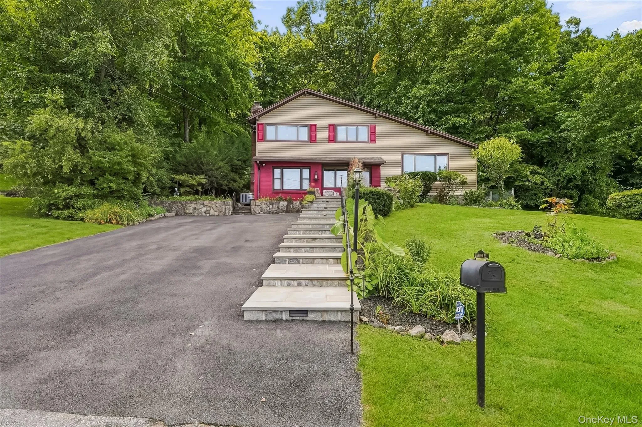 Split-level residence featuring a paved driveway, stone retaining walls, and a tiered stone walkway Split-level residence featuring a paved driveway, stone retaining walls, and a tiered stone walkway