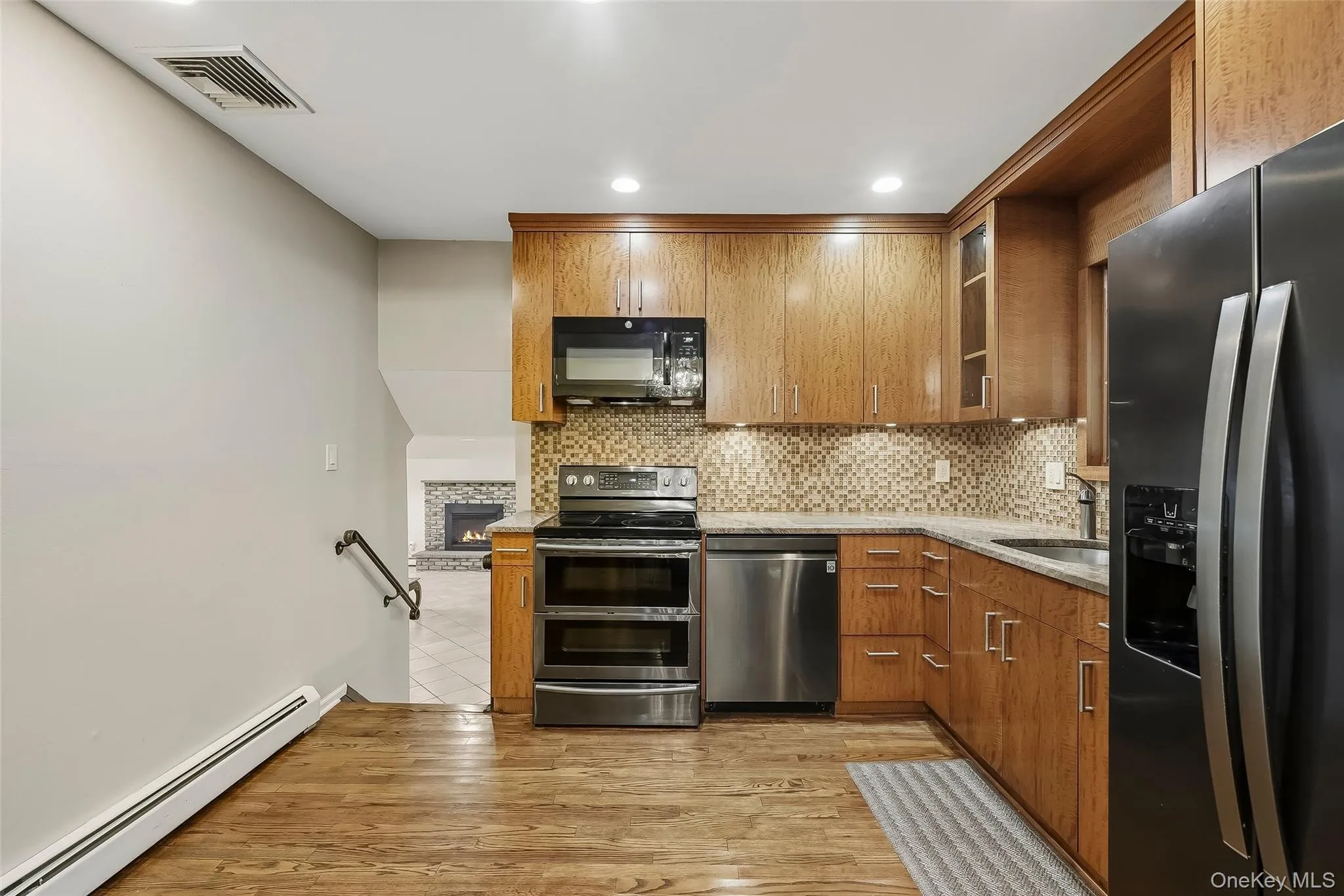 Kitchen with wood flooring featuring custom cabinetry, stainless steel appliances, and a tiled backsplash Kitchen with wood flooring featuring custom cabinetry, stainless steel appliances, and a tiled backsplash