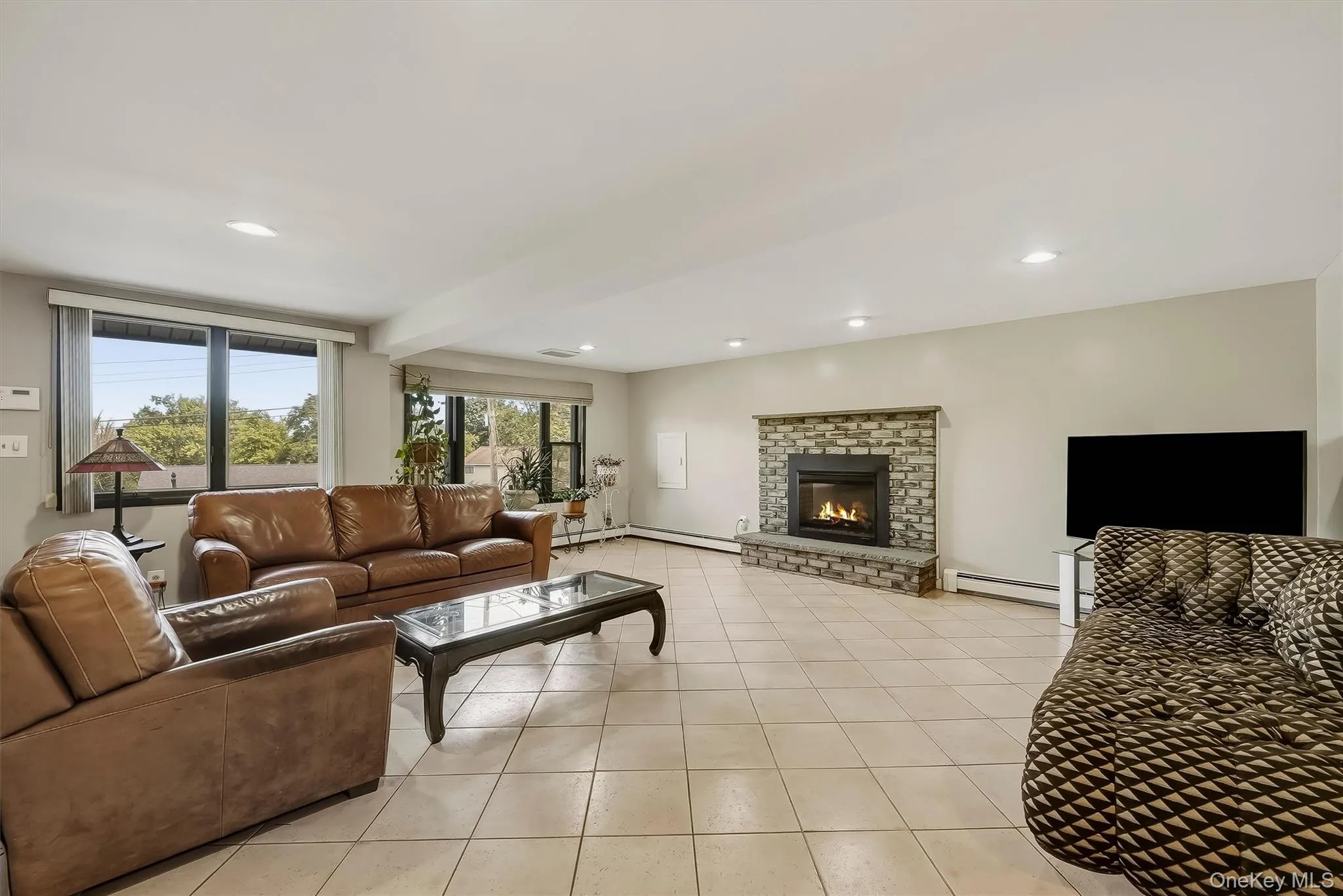 Spacious recreation room featuring tile flooring, a stone-clad fireplace, and recessed lighting Spacious recreation room featuring tile flooring, a stone-clad fireplace, and recessed lighting