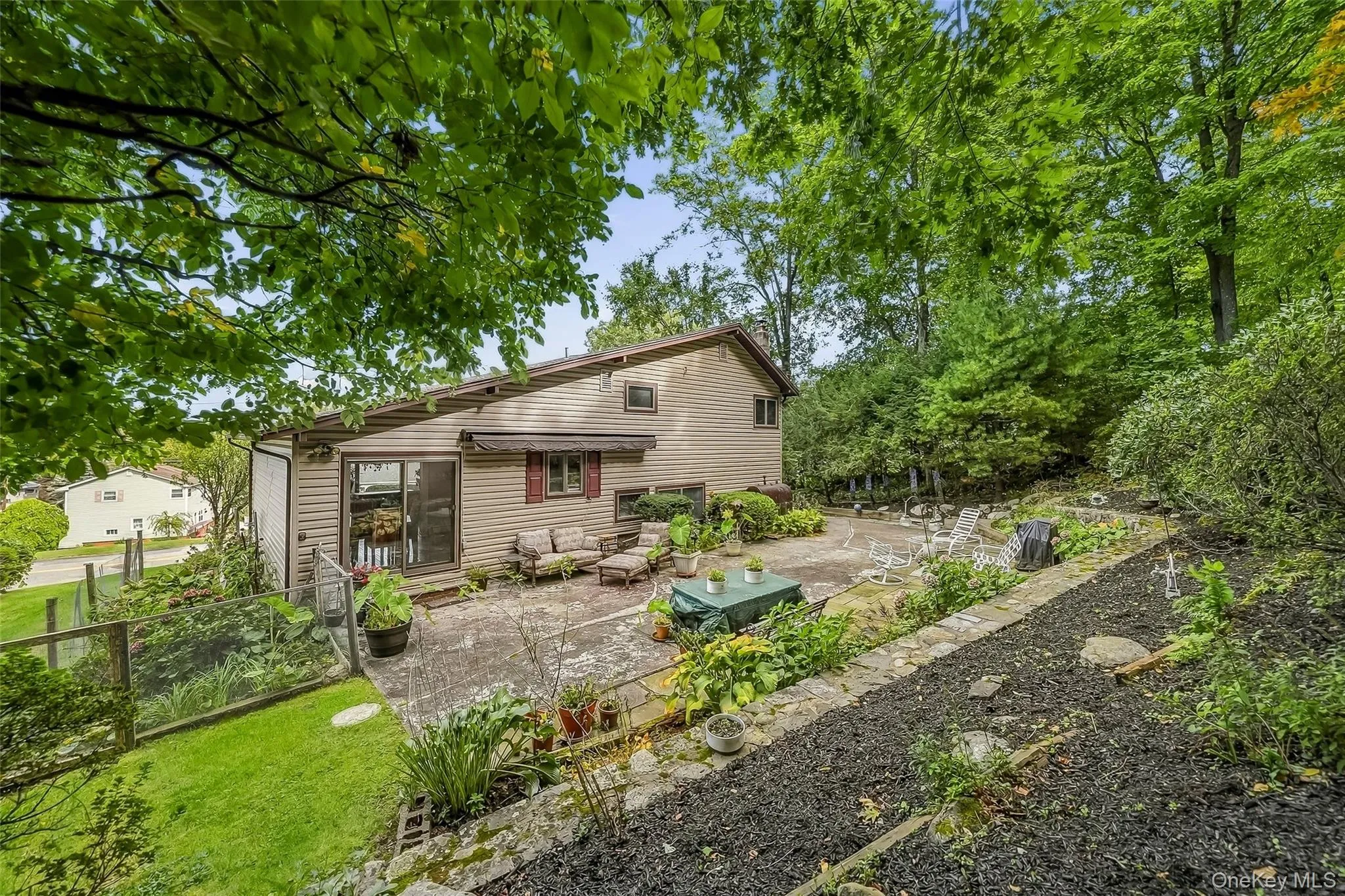 Expansive rear patio area featuring concrete paving, mature landscaping, and a tiered, mulched garden bed Expansive rear patio area featuring concrete paving, mature landscaping, and a tiered, mulched garden bed