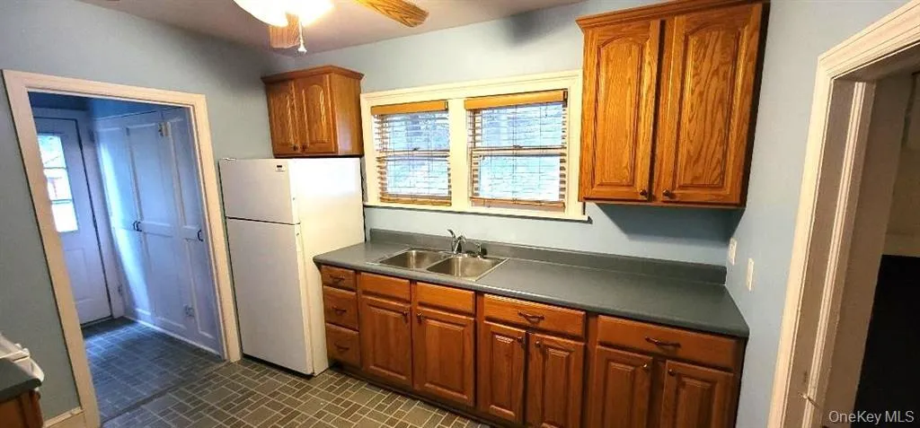 Kitchen with sink, dark tile patterned floors, white refrigerator, and ceiling fan Kitchen with sink, dark tile patterned floors, white refrigerator, and ceiling fan