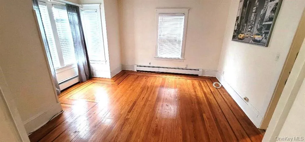 Unfurnished room with a baseboard radiator, plenty of natural light, and hardwood / wood-style floors Unfurnished room with a baseboard radiator, plenty of natural light, and hardwood / wood-style floors