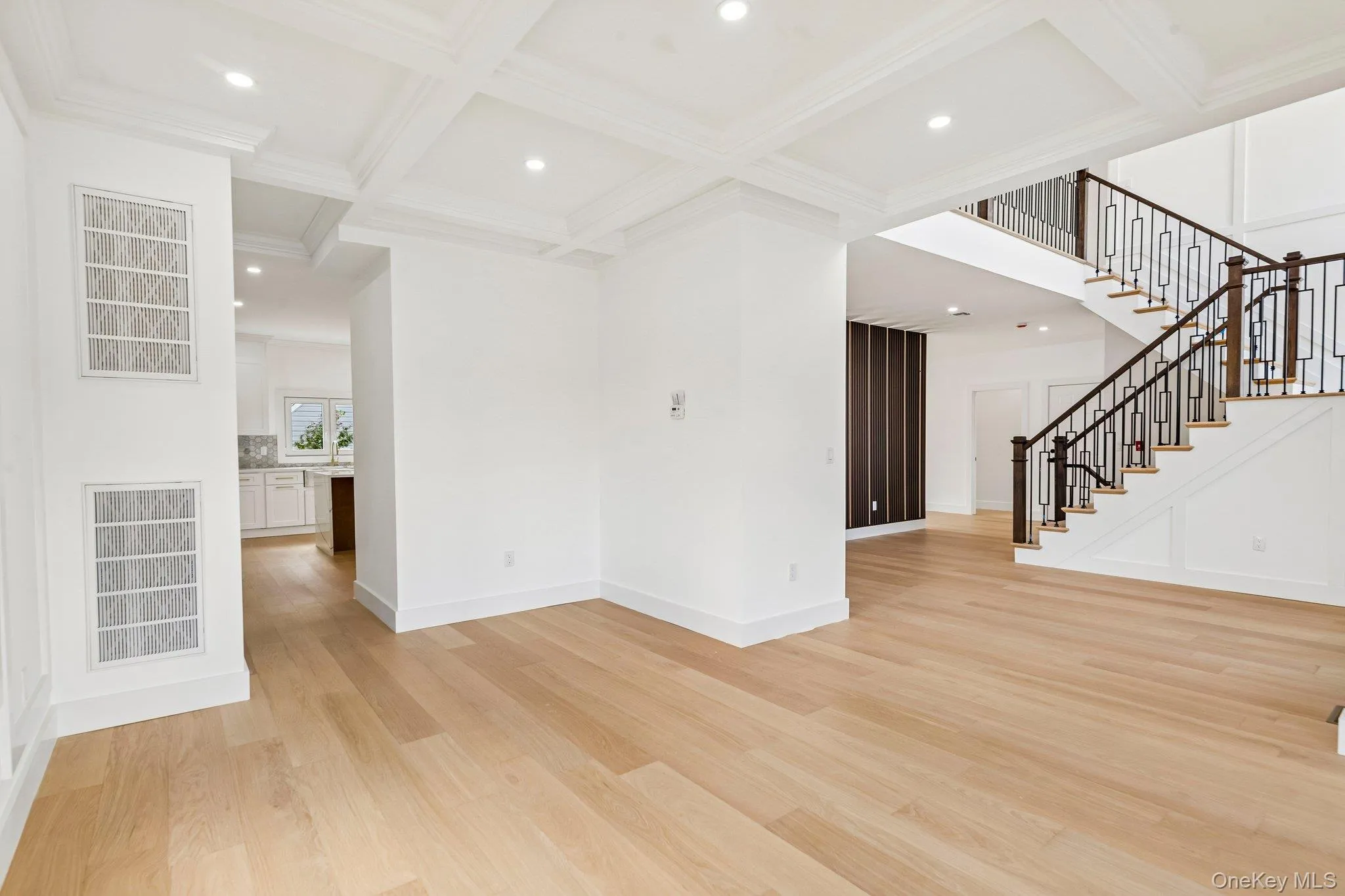 Light wood-finish flooring, coffered ceiling with recessed lighting, and a staircase featuring dark wood handrails with decorative metal balusters Light wood-finish flooring, coffered ceiling with recessed lighting, and a staircase featuring dark wood handrails with decorative metal balusters