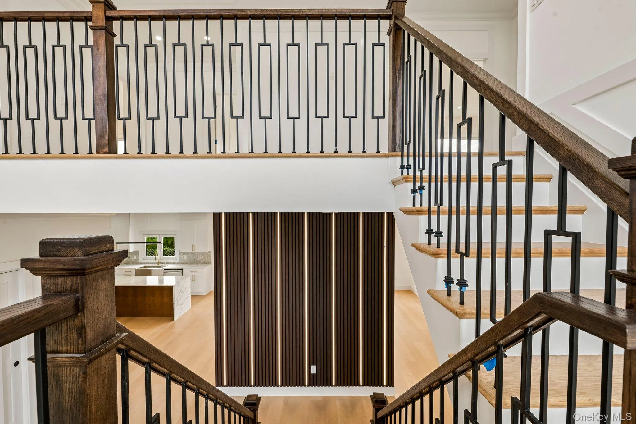 Wood-finish staircase with black metal balusters, hardwood flooring, and a decorative slatted wall panel Wood-finish staircase with black metal balusters, hardwood flooring, and a decorative slatted wall panel