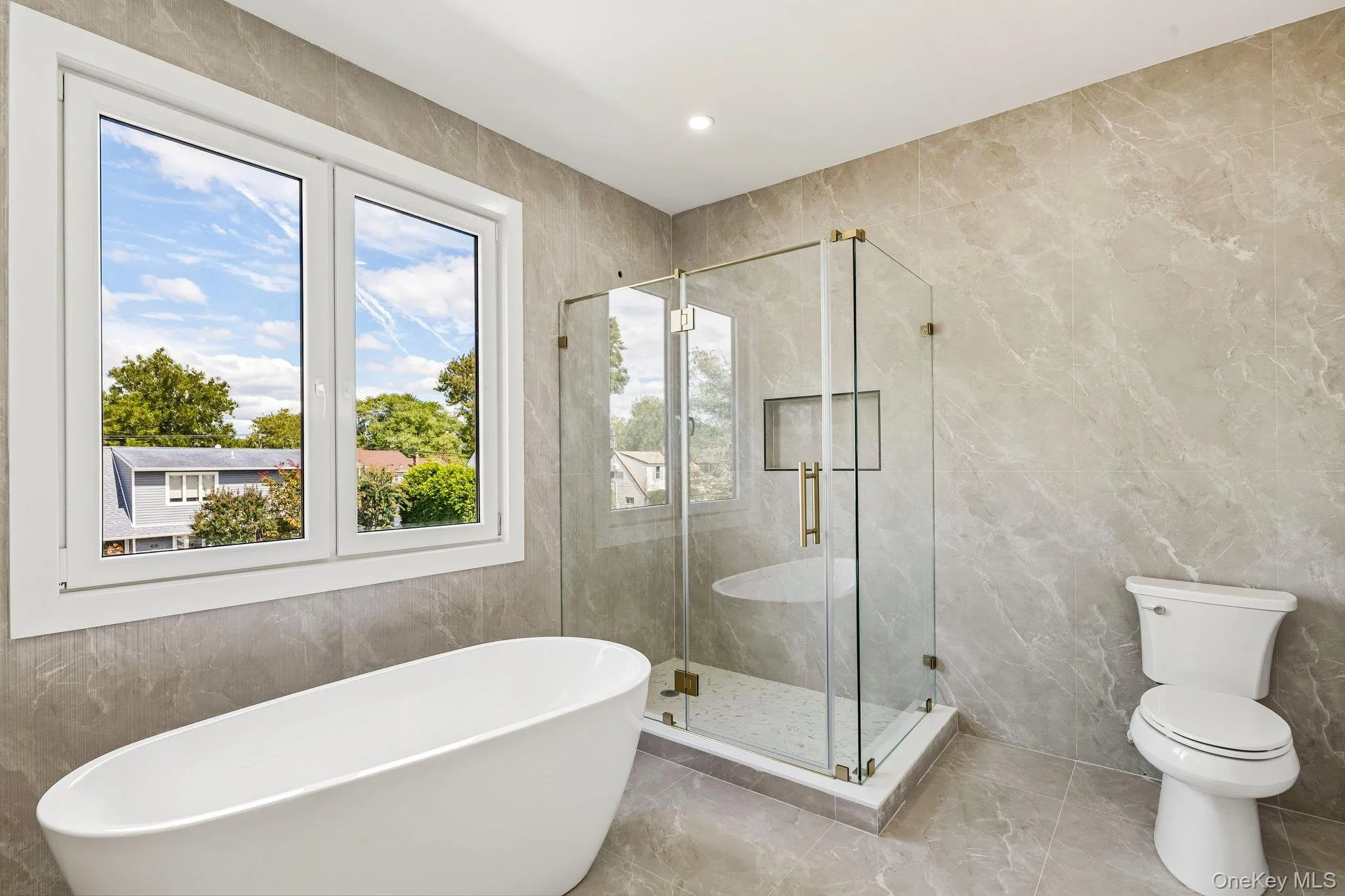 Freestanding soaking tub, glass-enclosed shower with built-in bench, recessed shower niche, contemporary wall tiles, and large window with white trim Freestanding soaking tub, glass-enclosed shower with built-in bench, recessed shower niche, contemporary wall tiles, and large window with white trim